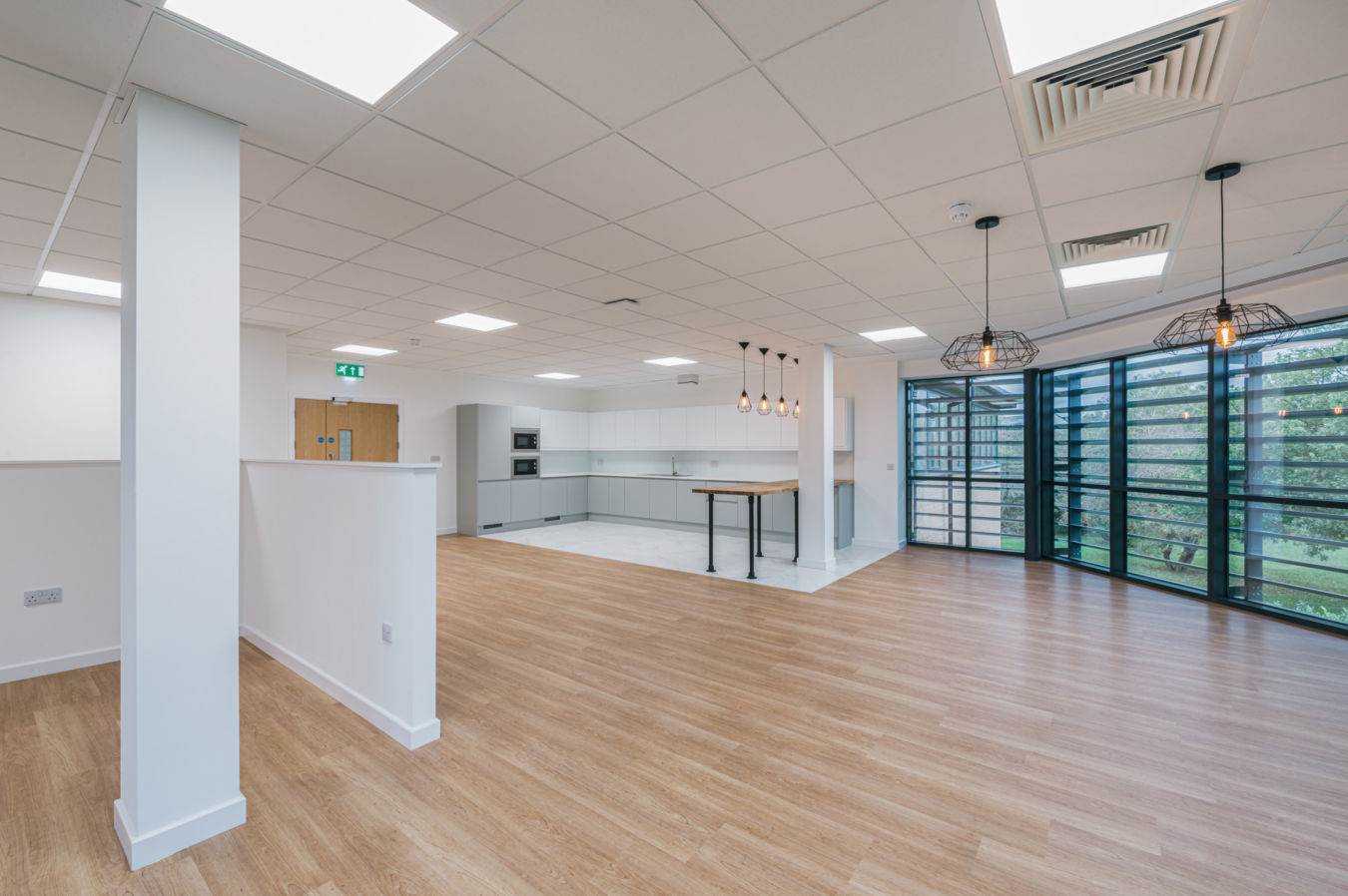 Spacious modern kitchen features white cabinets, a wooden island, and pendant lights, set in a well-lit room with wood flooring and large windows overlooking greenery.