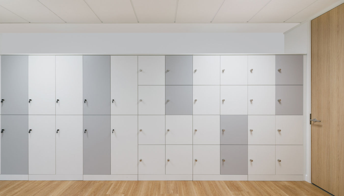 wall of modern, multi-colored lockers in shades of white and gray with wooden handles. The floor is light wood, and a wooden door is on the right