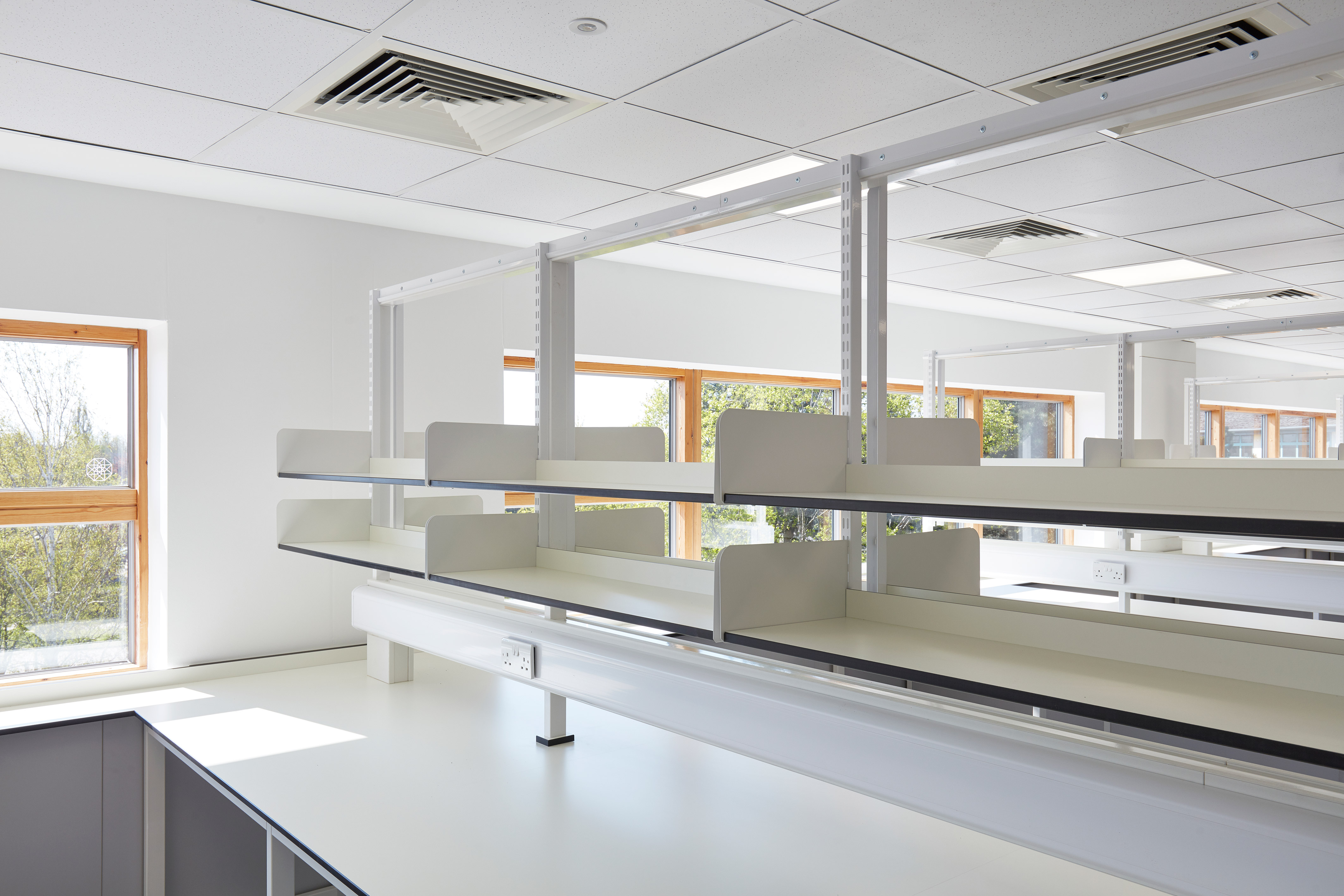 Bright laboratory space with white countertops, dual-sided shelving, and large windows allowing natural light into the room