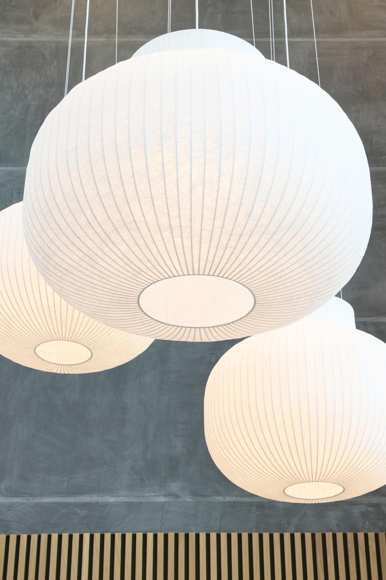 Three large, white, spherical pendant lights hang from a ceiling, casting soft light over a modern space with gray walls and wooden accents.