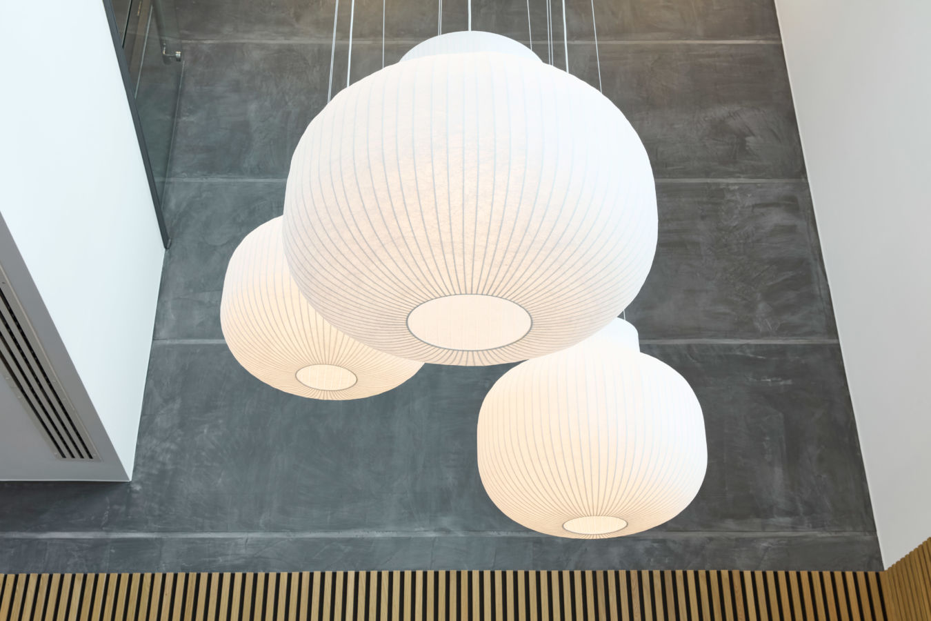 Three large, white, spherical pendant lights hang from a ceiling, casting soft light over a modern space with gray walls and wooden accents.