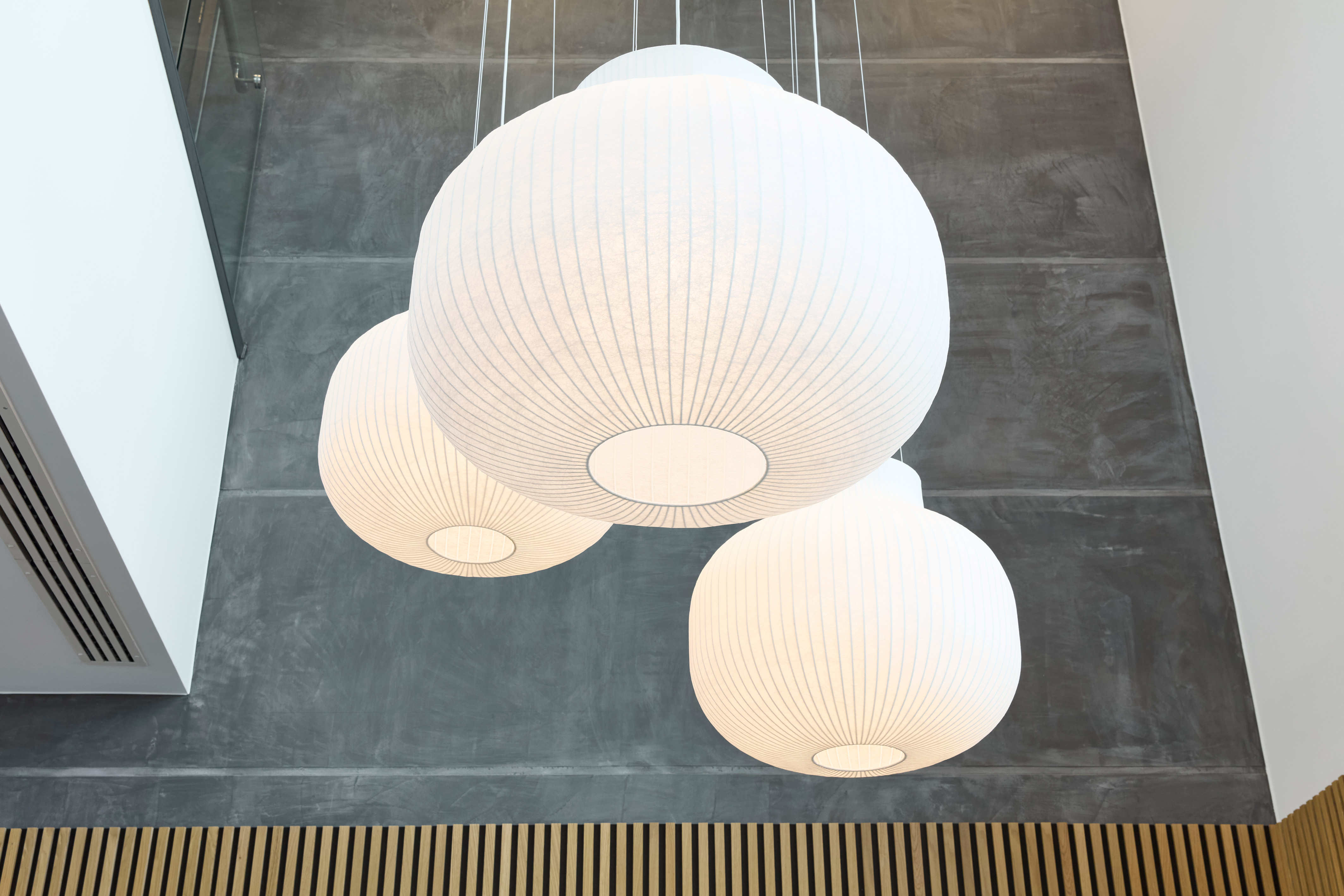 Three large, white, spherical pendant lights hang from a ceiling, casting soft light over a modern space with gray walls and wooden accents.