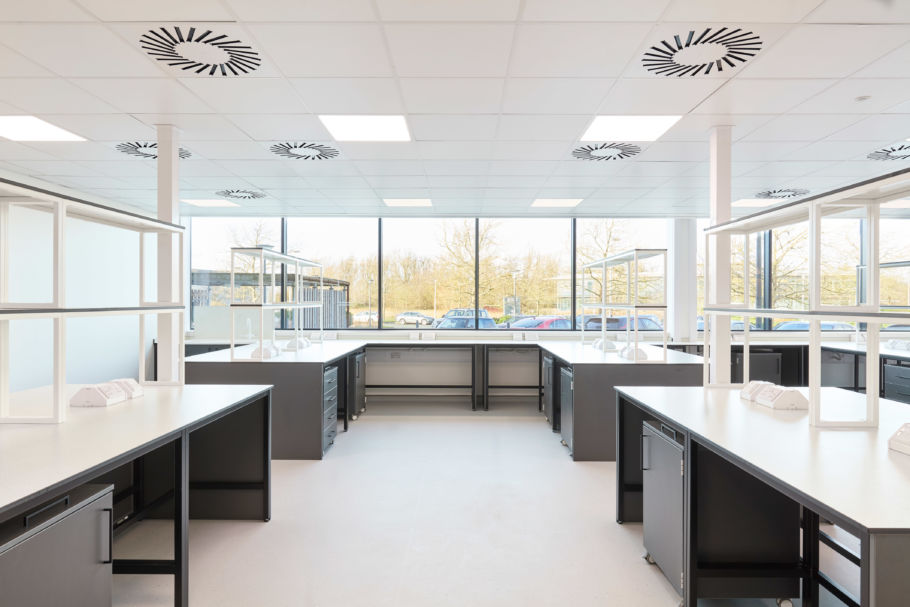 Bright and spacious laboratory with large windows, black and white workbenches, ceiling-mounted ventilation units, and natural light filling the room.