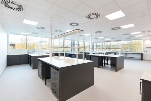 Modern laboratory with black workbenches, white countertops, overhead shelving, and large windows allowing in abundant natural light.