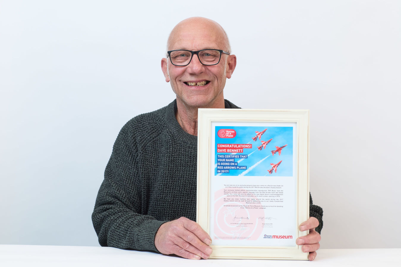 A person holding a framed certificate, smiling against a plain background. The certificate reads: "CONGRATULATIONS! DAVE BENNETT, THIS CERTIFIES THAT YOUR NAME IS GOING ON A RED ARROWS PLANE IN 2017."