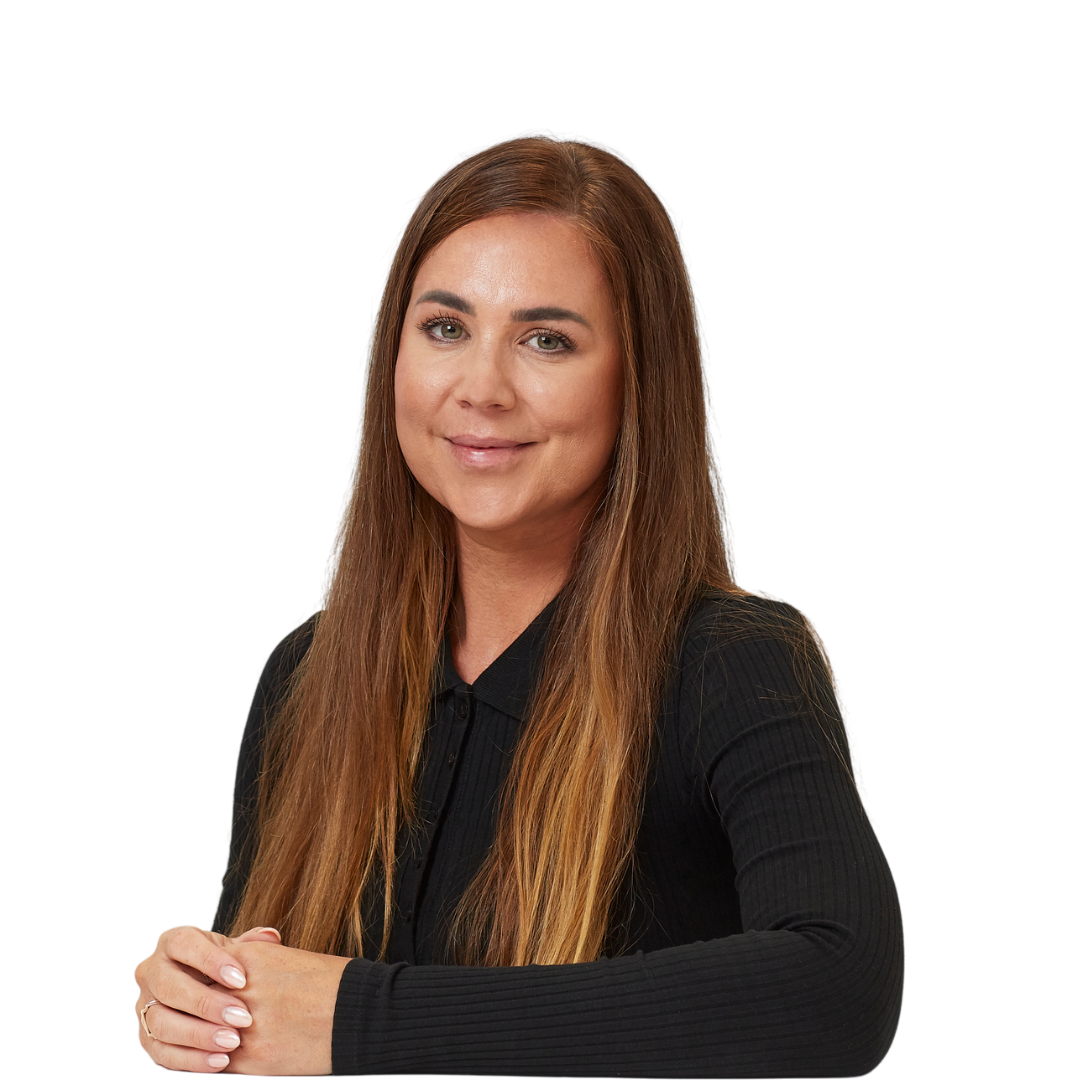 A person with long brown hair smiles gently while seated with hands clasped, wearing a black top, against a plain white background.