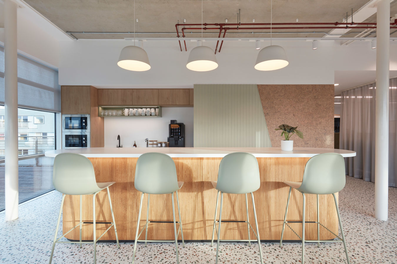 Modern kitchen with light wood cabinetry, four sleek sage-green bar stools, and pendant lights. Clean lines and neutral tones create a calm atmosphere