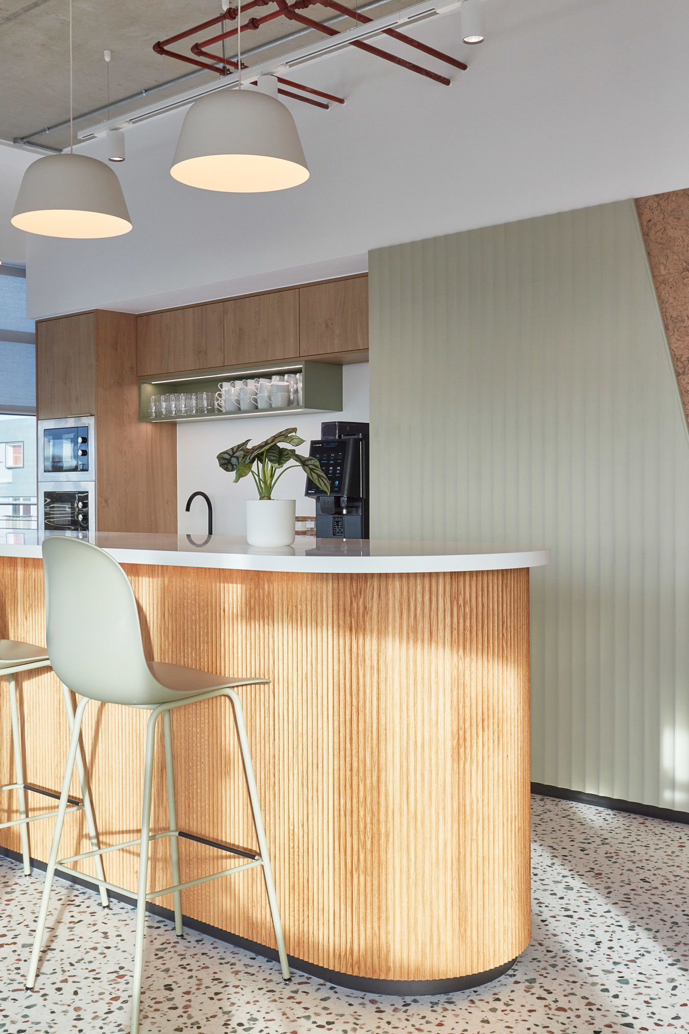 A modern kitchen features a wooden island with fluted design, a white countertop, and bar stools; pendant lights hang above, with shelves displaying mugs, a faucet, and a potted plant.