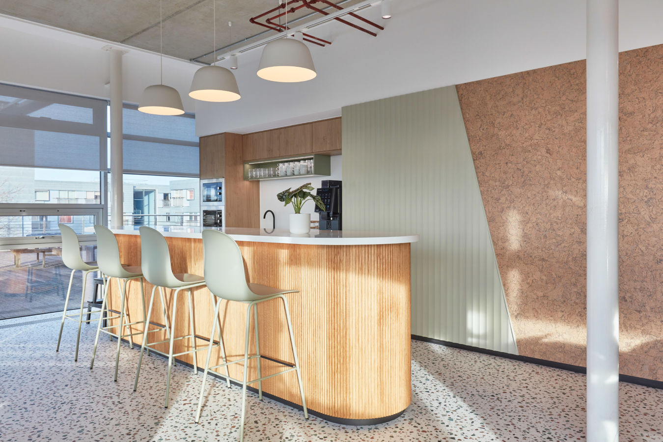 A modern kitchen features a wooden island with fluted design, a white countertop, and bar stools; pendant lights hang above, with shelves displaying mugs, a faucet, and a potted plant.