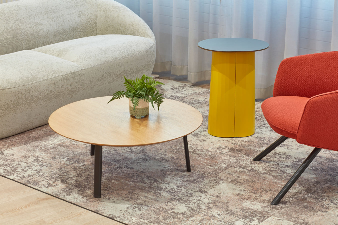 Close-up of a modern lounge area featuring a round wooden coffee table with a potted plant, a yellow side table, and contemporary seating.