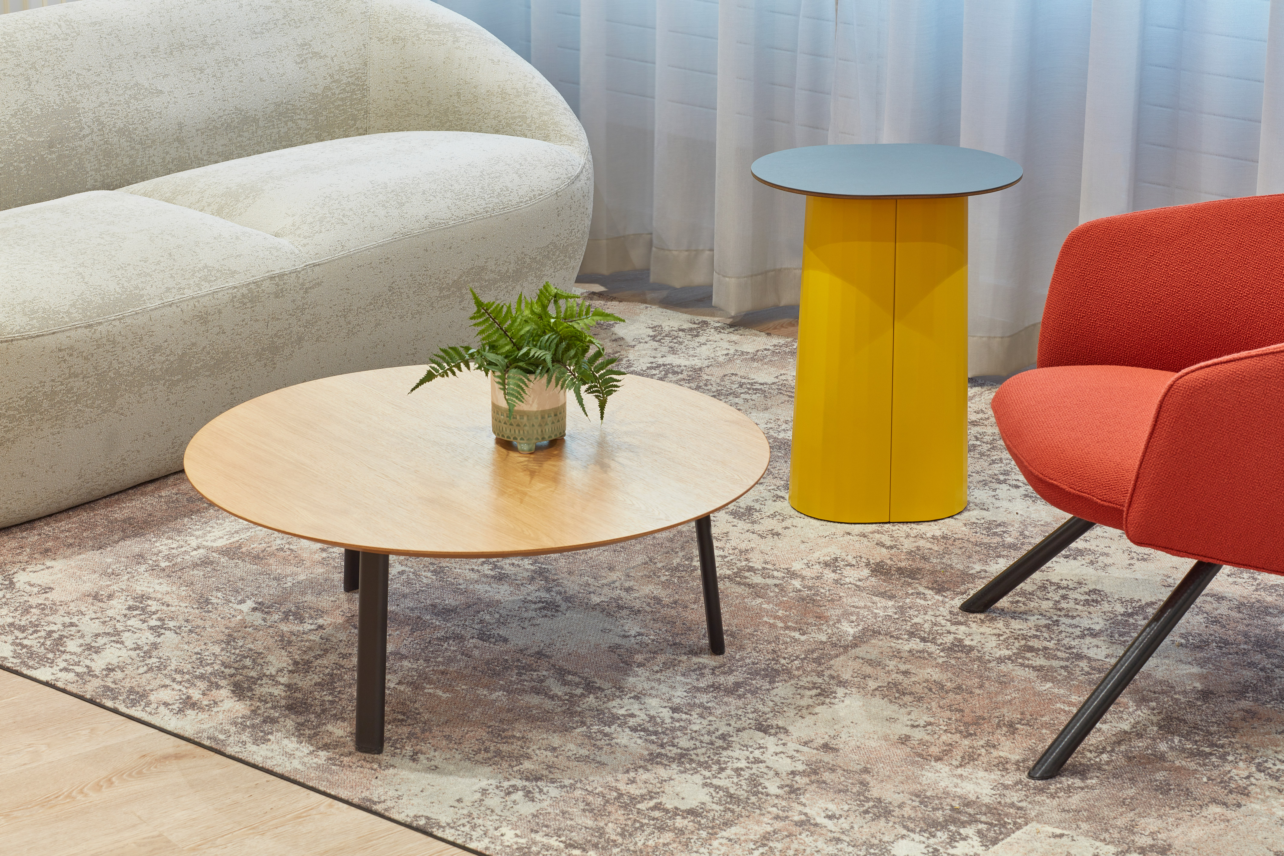 Close-up of a modern lounge area featuring a round wooden coffee table with a potted plant, a yellow side table, and contemporary seating.