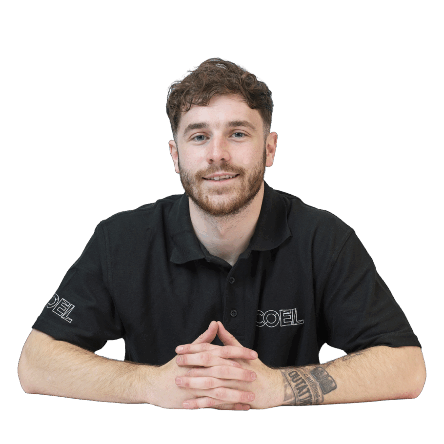Man sitting with hands clasped, wearing a black polo shirt with "COEL" logo on sleeves, displaying a tattoo on his left forearm, against a plain white background.