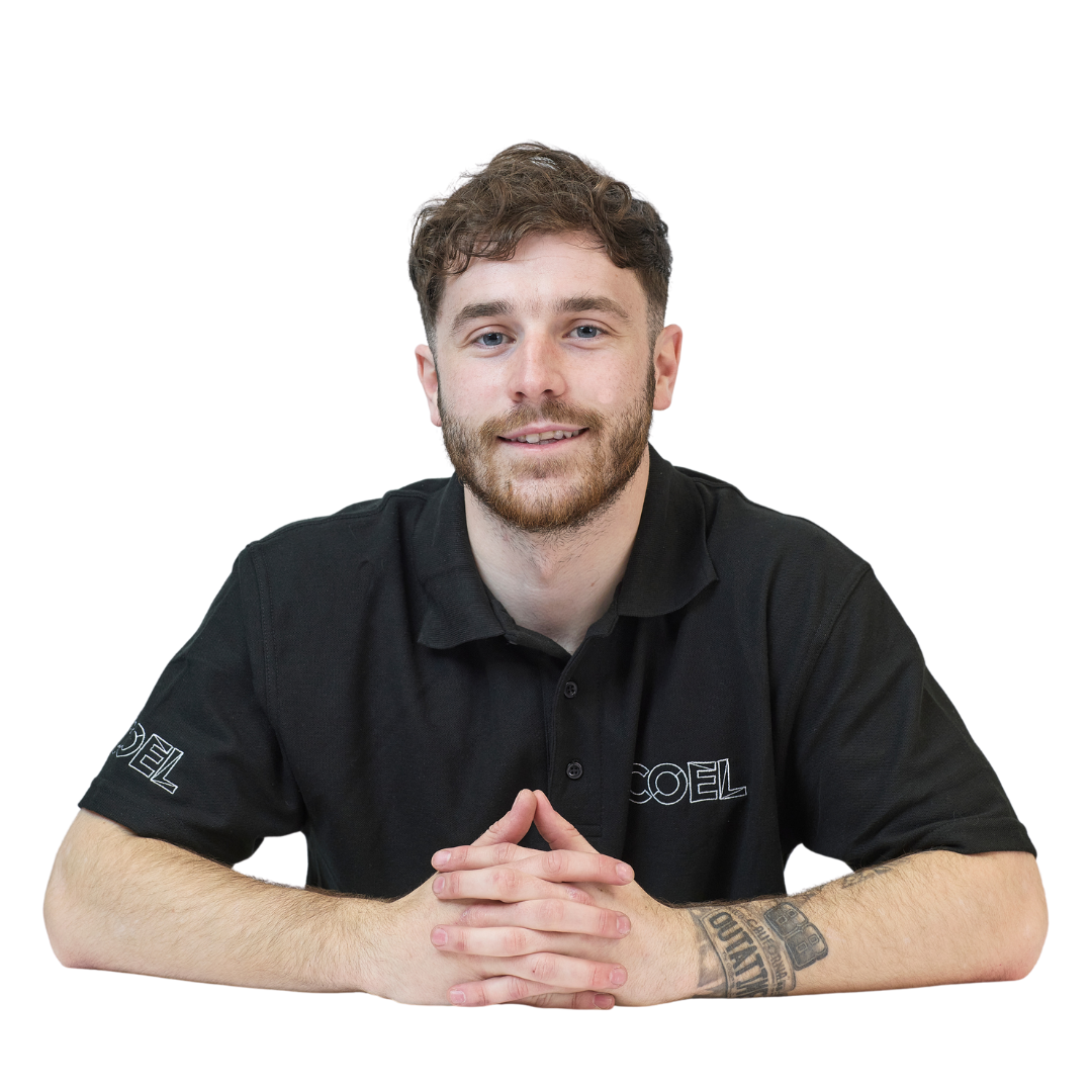 Man sitting with hands clasped, wearing a black polo shirt with "COEL" logo on sleeves, displaying a tattoo on his left forearm, against a plain white background.