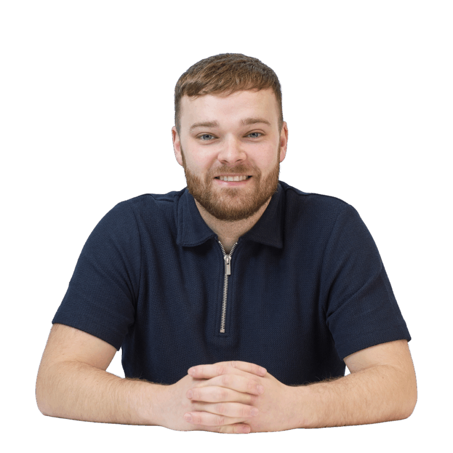 Smiling person sits at a table with hands clasped, wearing a navy polo shirt with a zipper, isolated on a plain white background.