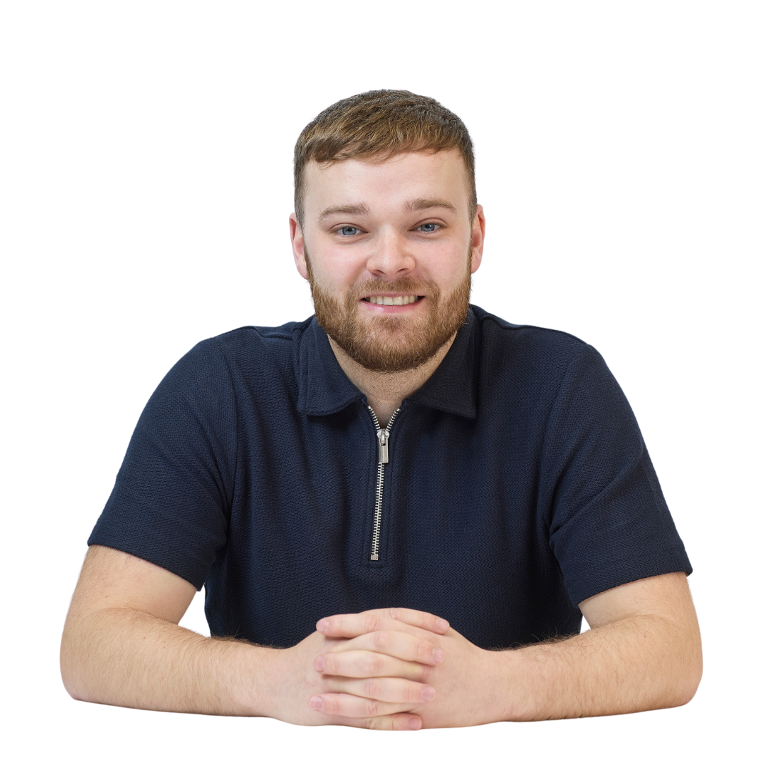 Smiling person sits at a table with hands clasped, wearing a navy polo shirt with a zipper, isolated on a plain white background.