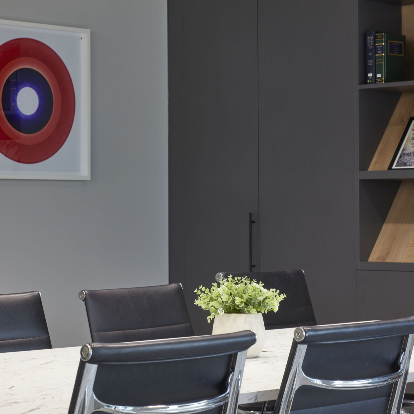 A potted plant sits on a white marble table surrounded by black leather chairs in a modern office setting with a partial view of a red artwork on the wall.