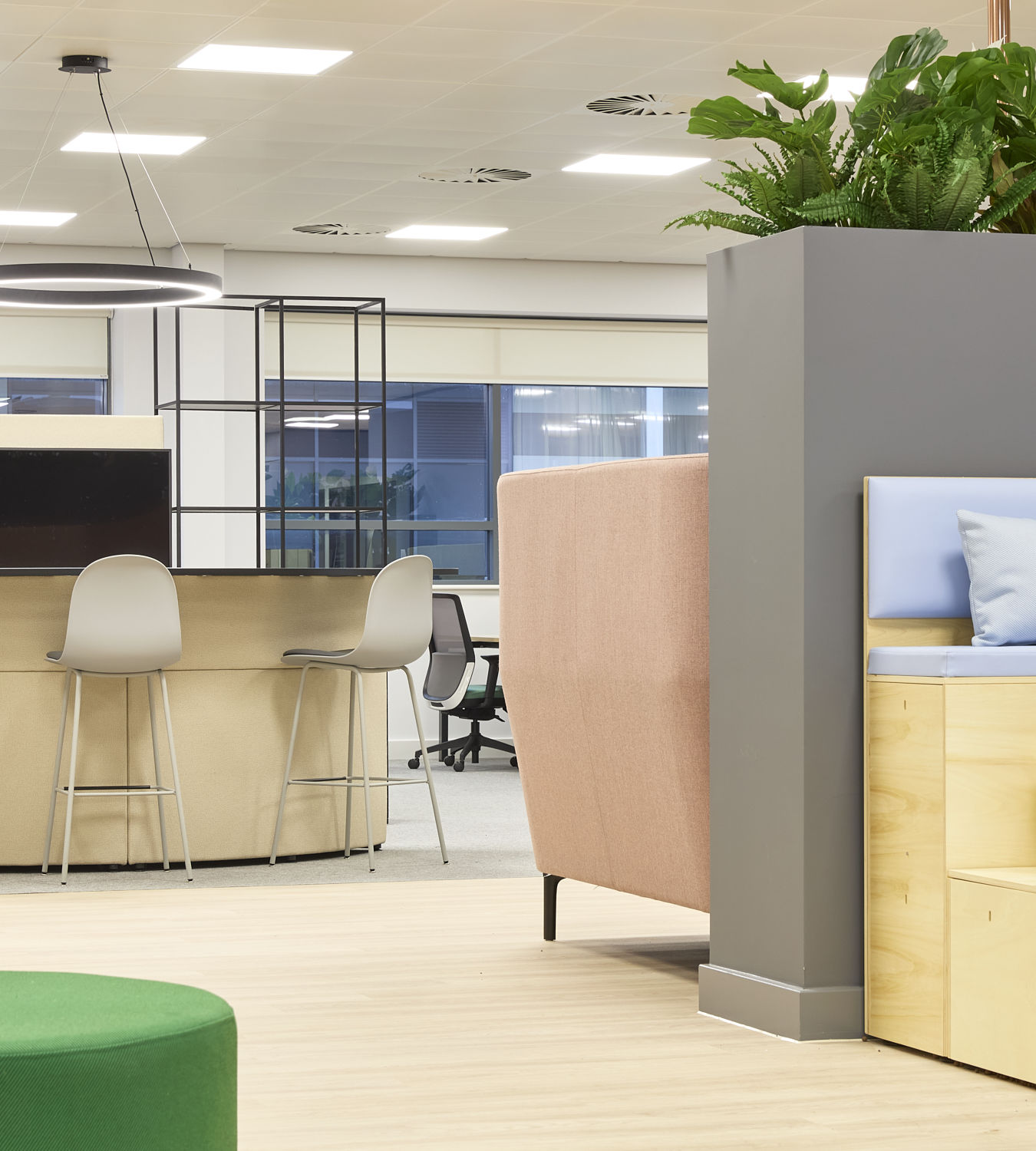 Open-plan office with mixed seating, high counter stools, soft furnishings, indoor plants, and modern lighting