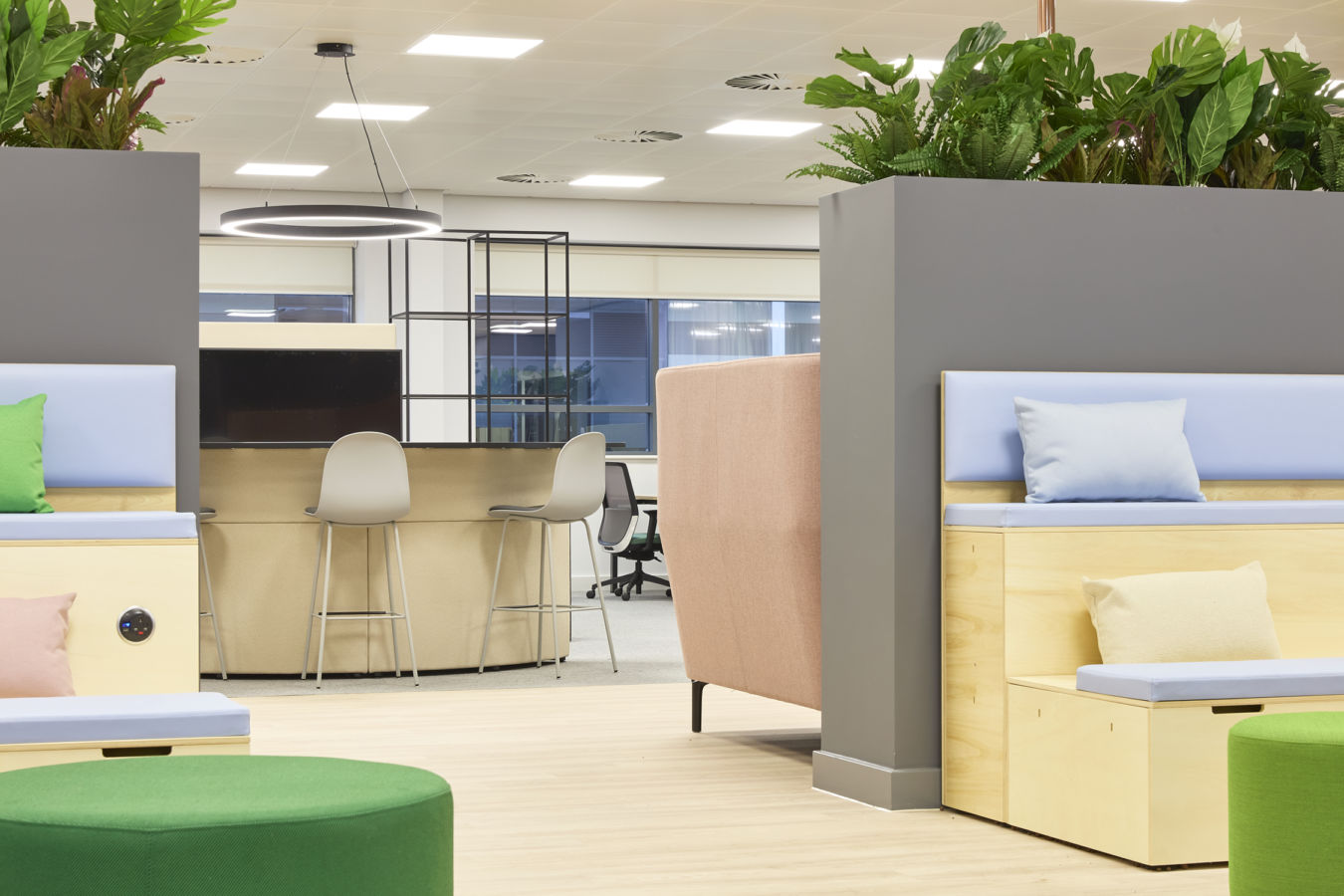 Open-plan office with mixed seating, high counter stools, soft furnishings, indoor plants, and modern lighting