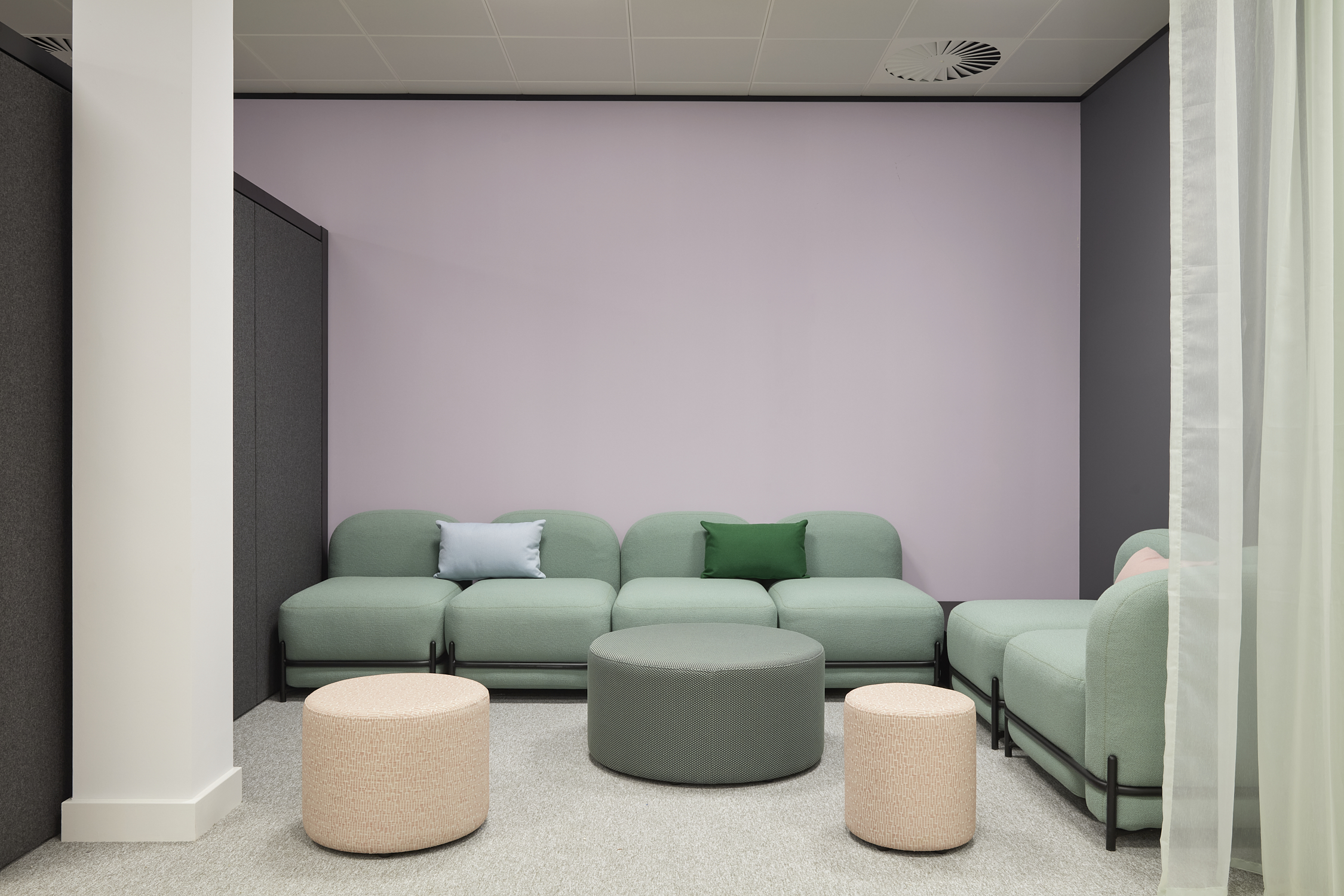 Minimalistic lounge with pastel green sectional sofa, light gray walls, and round ottomans. The setting feels soft and calm, inviting relaxation