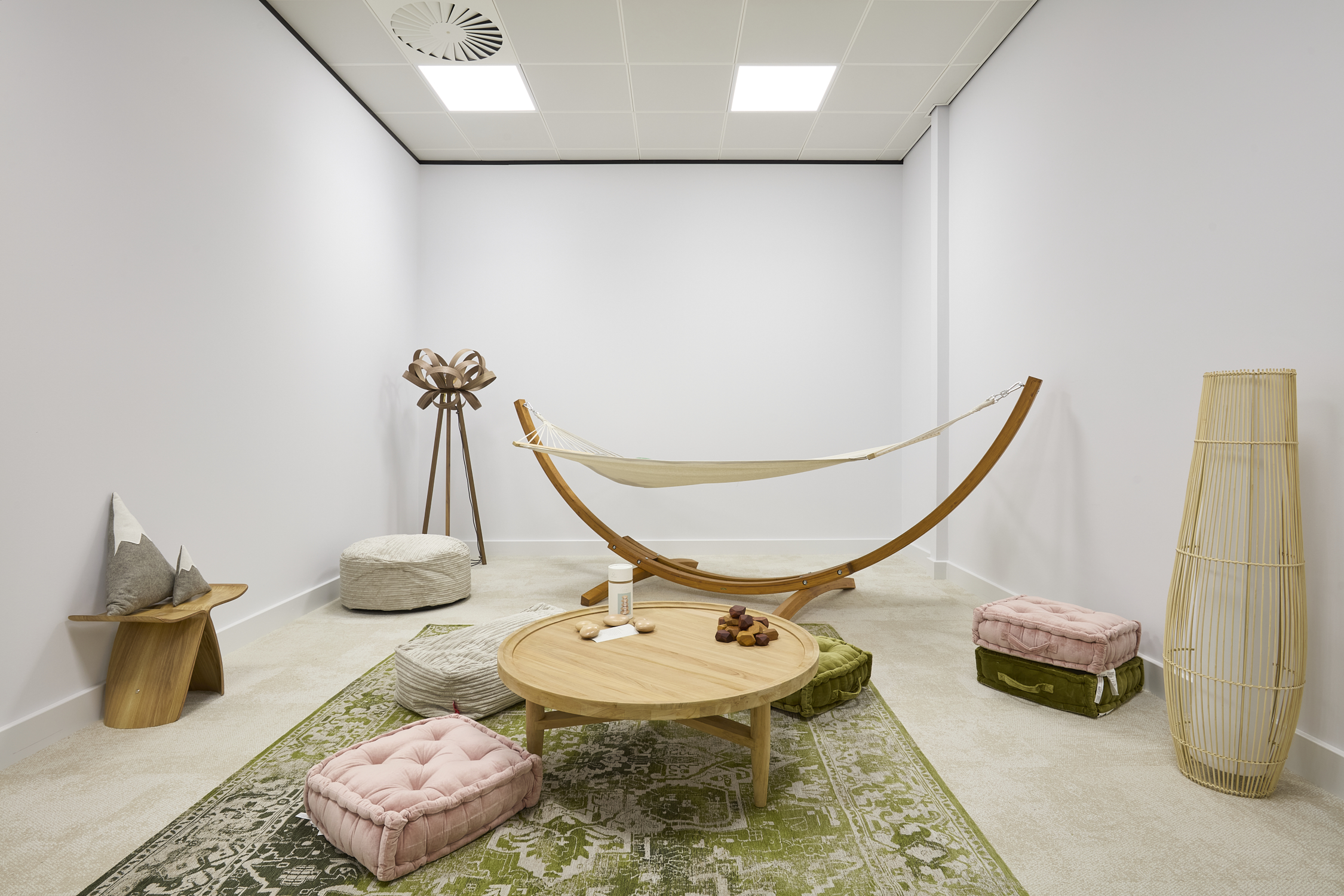 A hammock rests on a wooden stand in a minimalist room featuring cushioned seating.