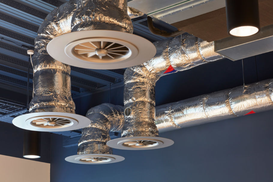 Ceiling ducts and vents with shiny metallic insulation and circular diffusers in a modern room. The industrial design is sleek and contemporary
