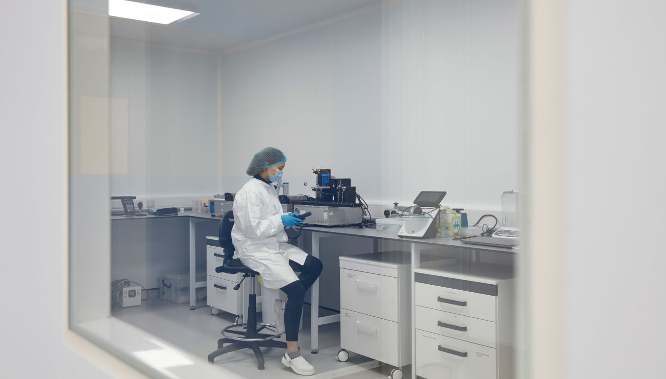 scientist in a lab coat and gloves works alone at a lab bench, surrounded by equipment and storage. The scene is calm and methodical
