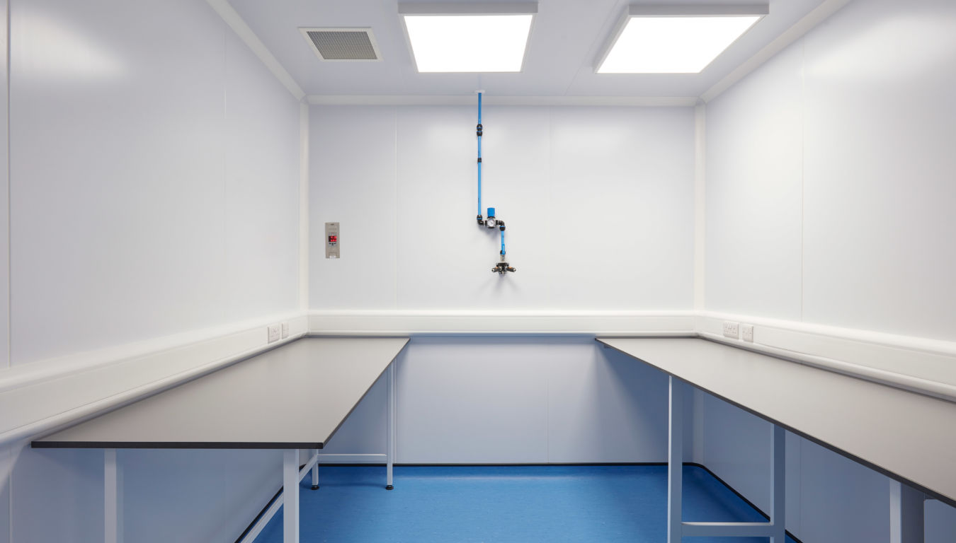 Sterile laboratory room with white walls, black worktops, bright overhead lighting, and a blue floor featuring a single mounted air or gas outlet.