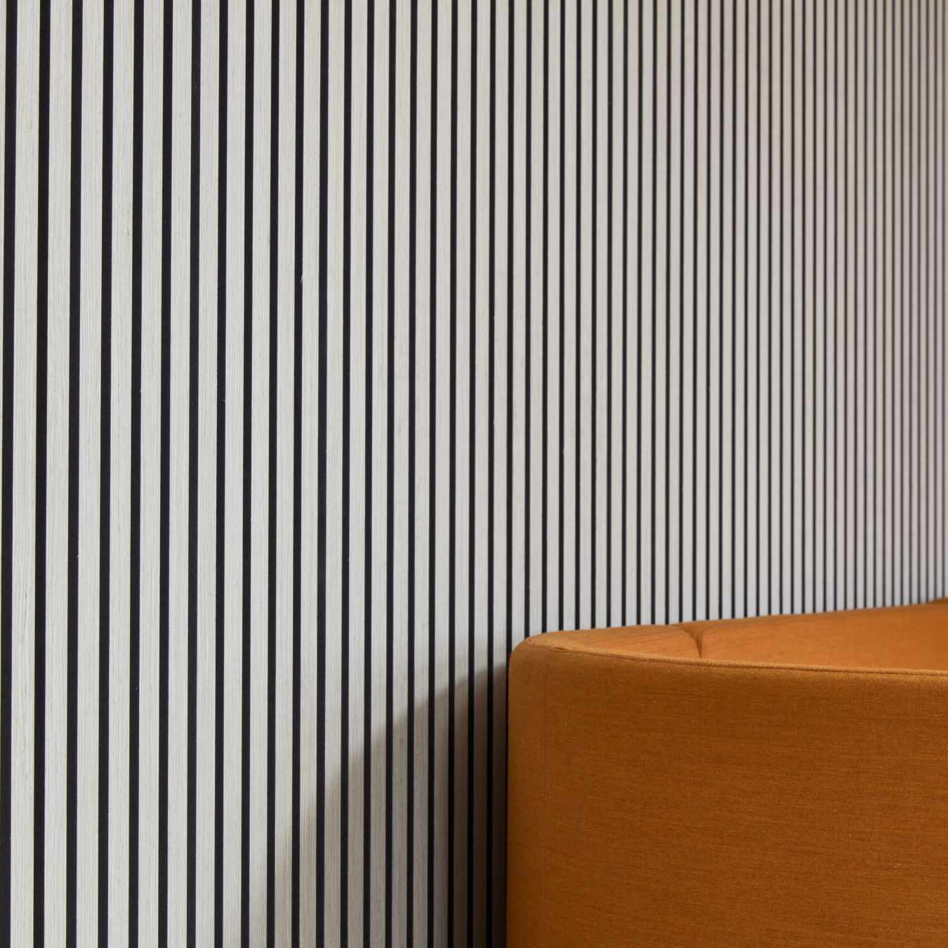 Orange upholstered couch curves against a wall with black and white vertical stripes, creating a modern, contrasting interior design setting.