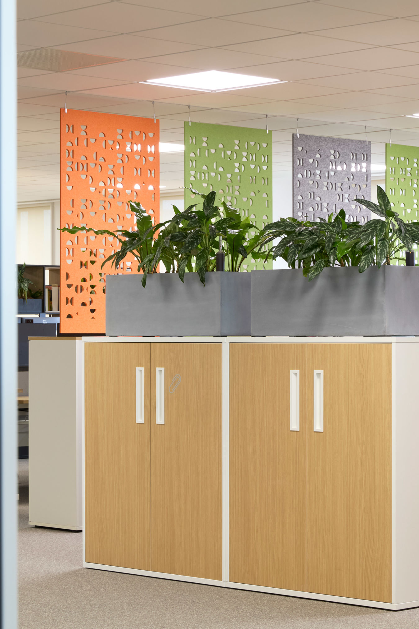 Office scene features plants on cabinets, surrounded by colorful panels and workstations with chairs and computers. Door labeled with the number "7" within sleek, modern workspace.