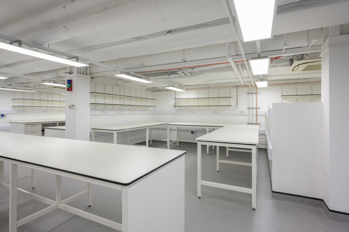 Bright, white laboratory space with multiple workbenches, open shelving, and exposed ceiling fixtures.