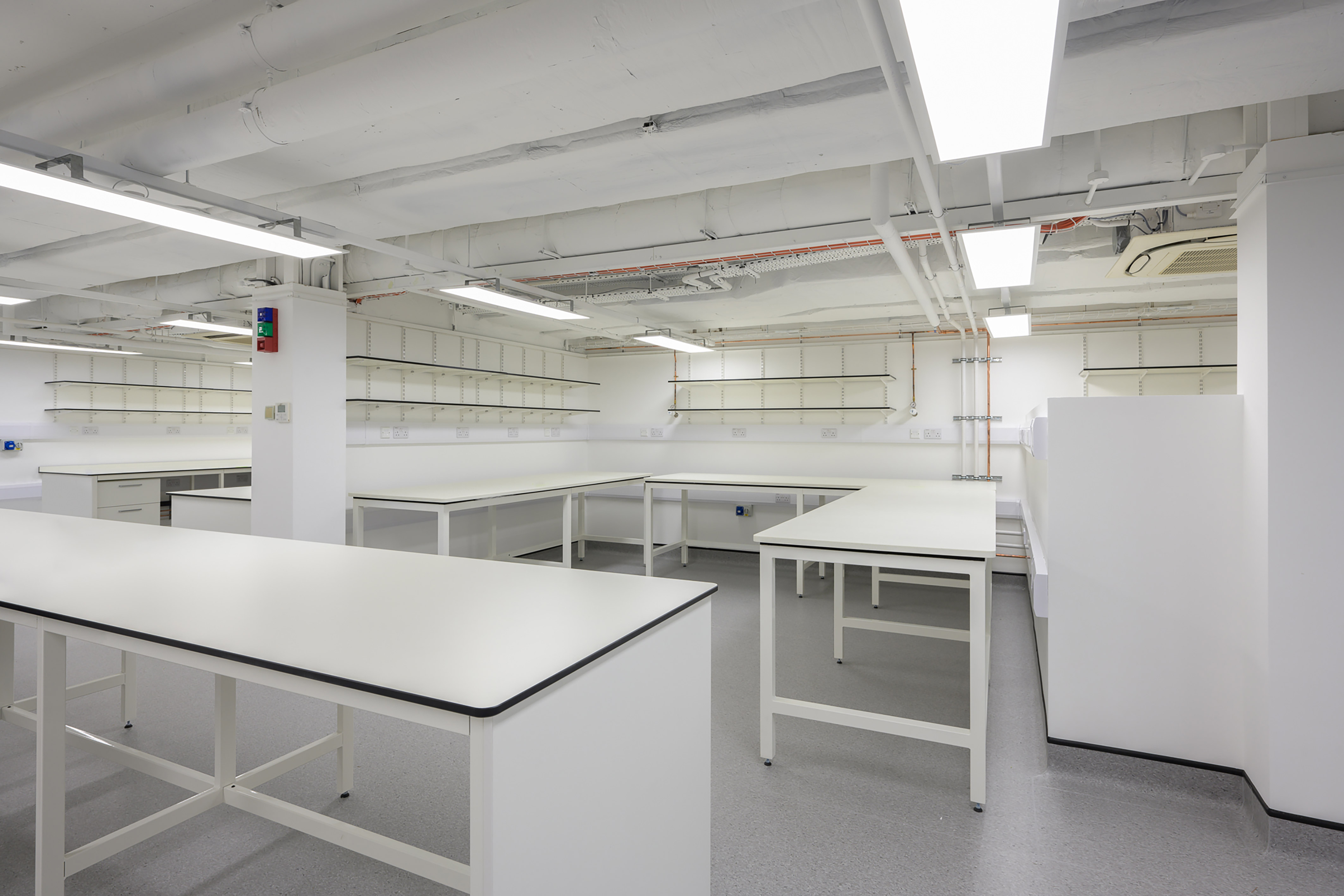 Bright, white laboratory space with multiple workbenches, open shelving, and exposed ceiling fixtures.