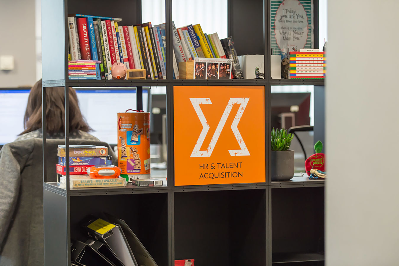 Open office shelving with books, branded merchandise, and decor, part of a COEL workspace fit-out for Jagex.