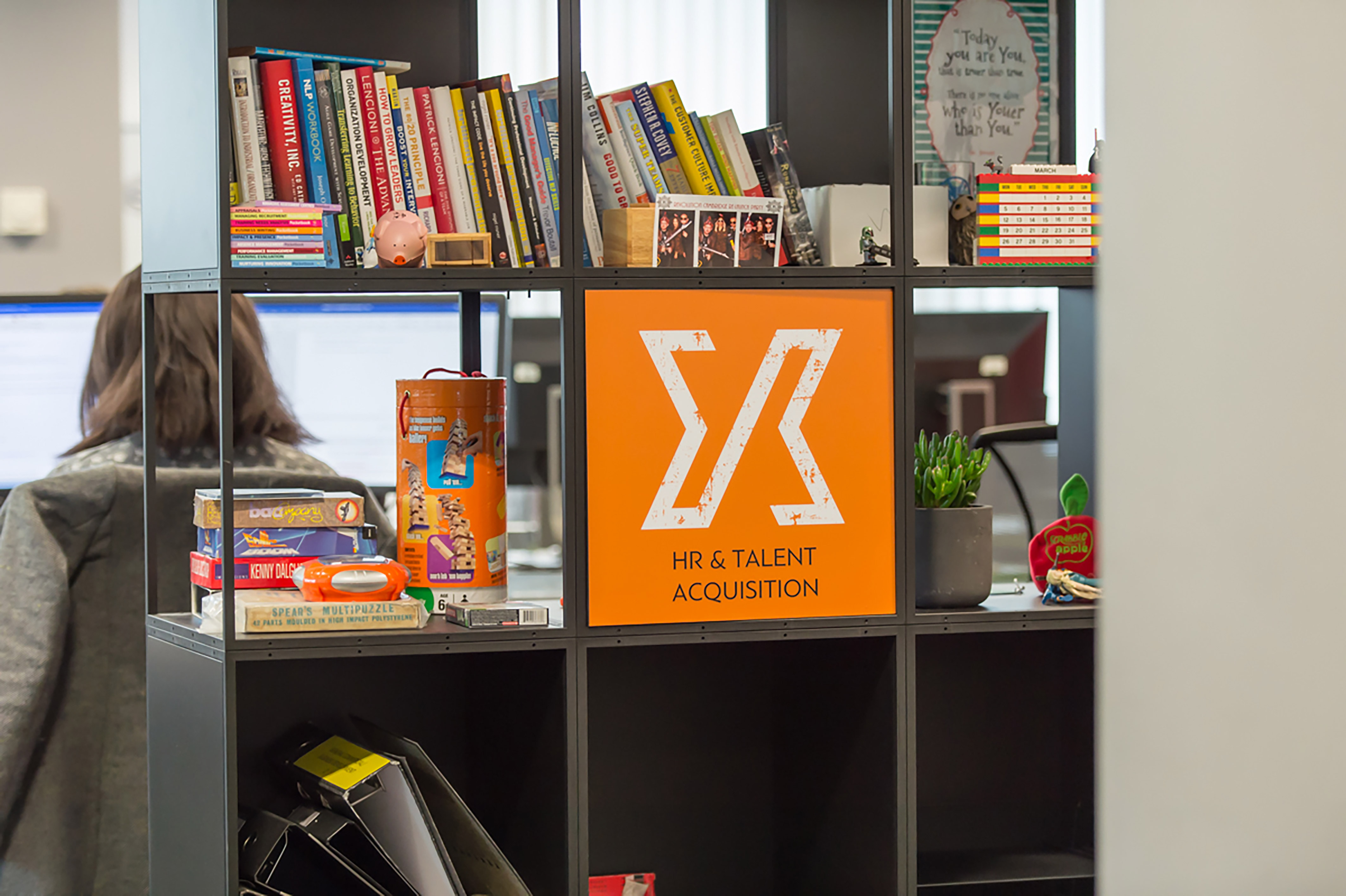 Open office shelving with books, branded merchandise, and decor, part of a COEL workspace fit-out for Jagex.