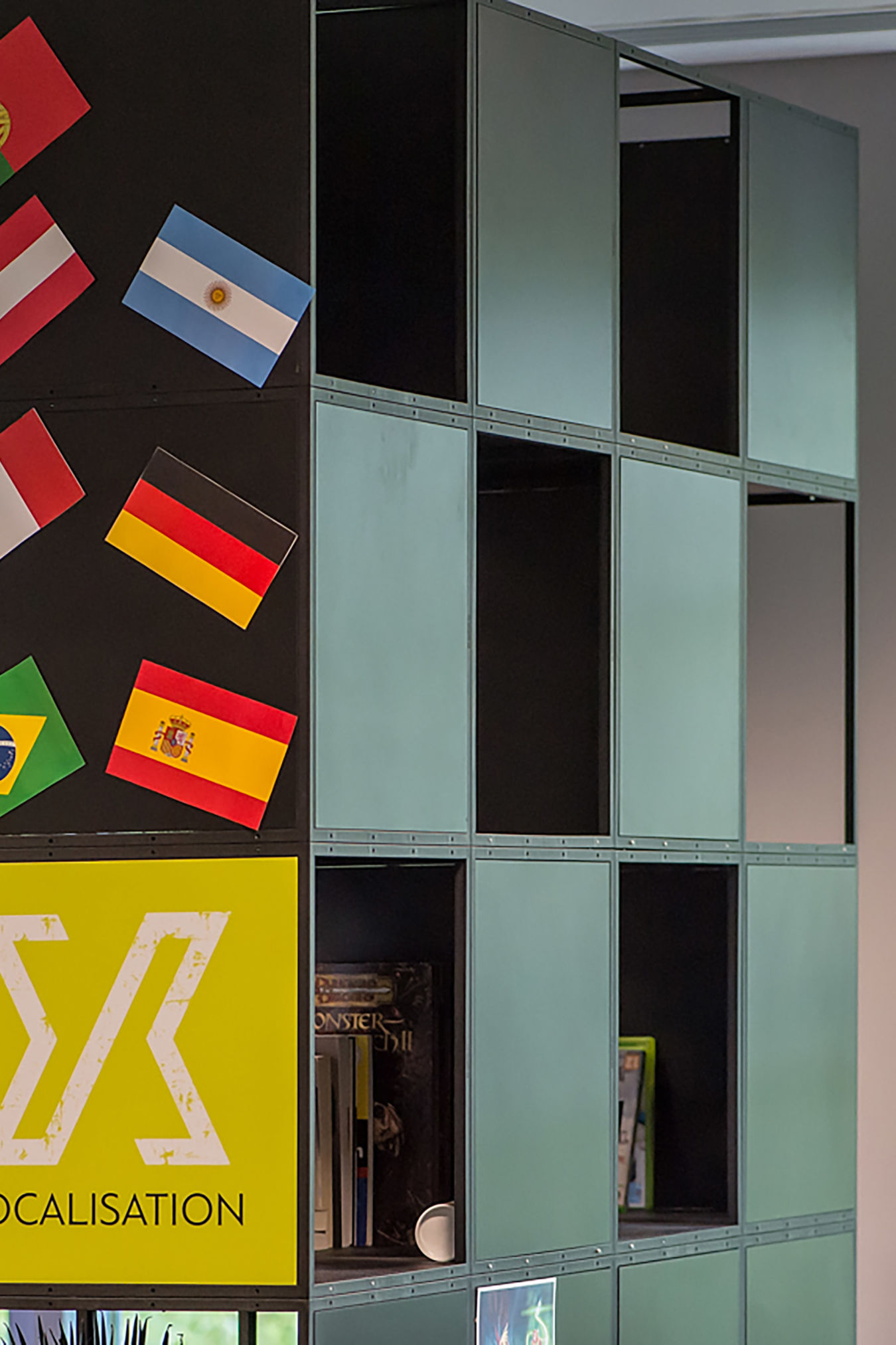 Cubical shelves displaying various items, featuring international flags and a yellow sign labeled "LOCALISATION," within an office environment.