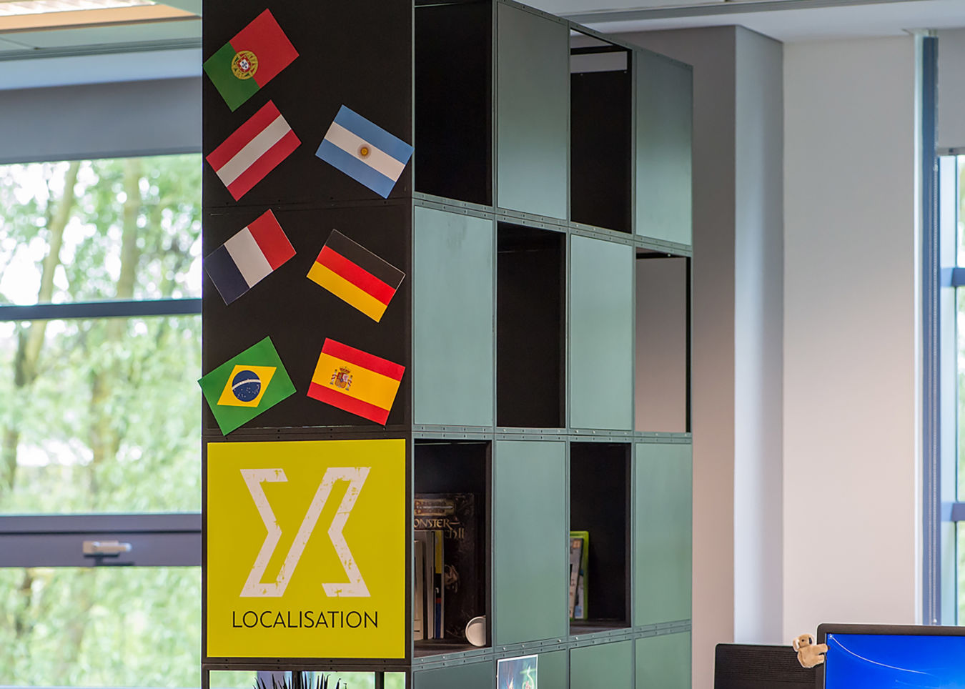 Cubical shelves displaying various items, featuring international flags and a yellow sign labeled "LOCALISATION," within an office environment.