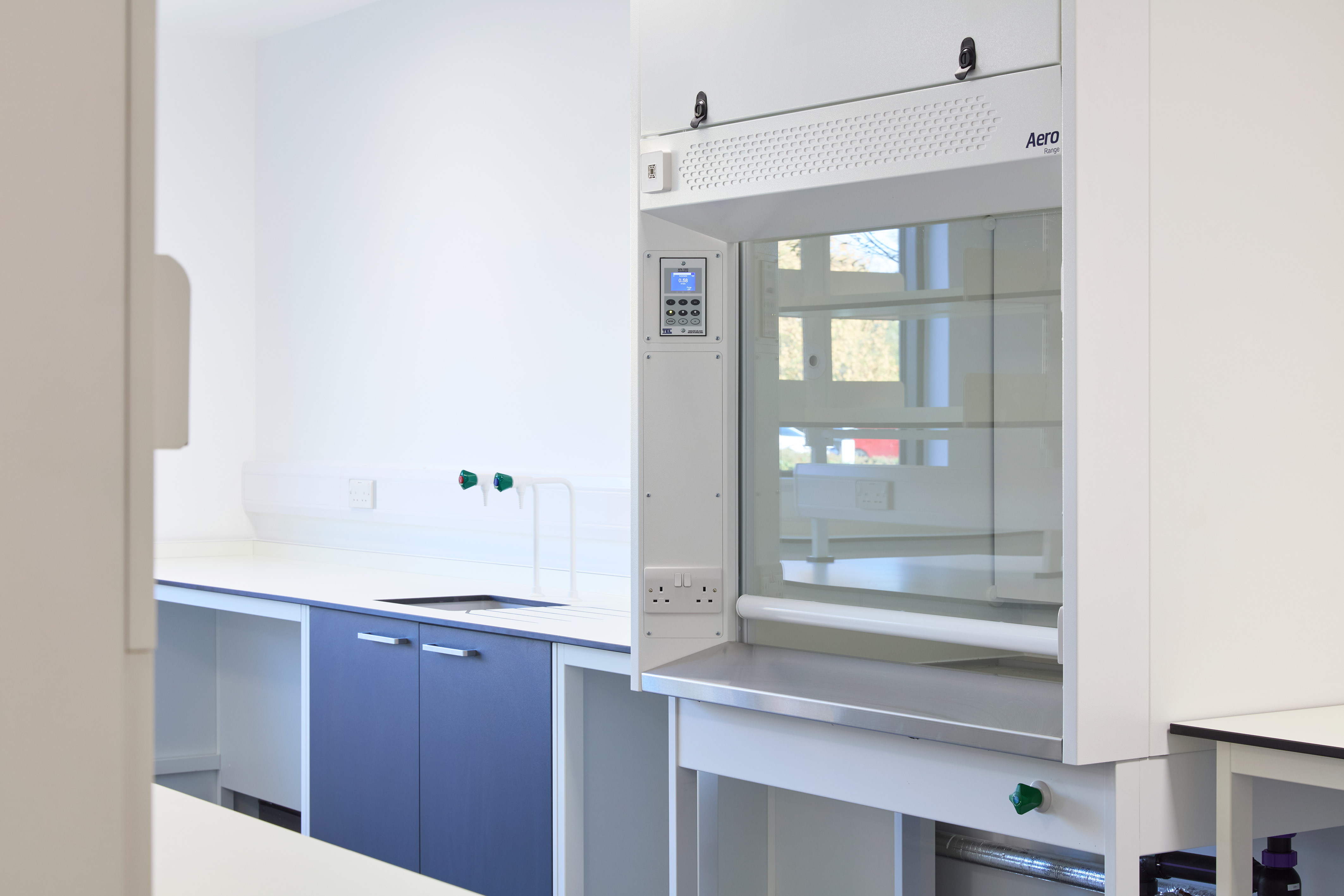 Modern laboratory with blue cabinets and a white fume hood on the right. Bright lighting and clean surfaces create a sterile, professional atmosphere