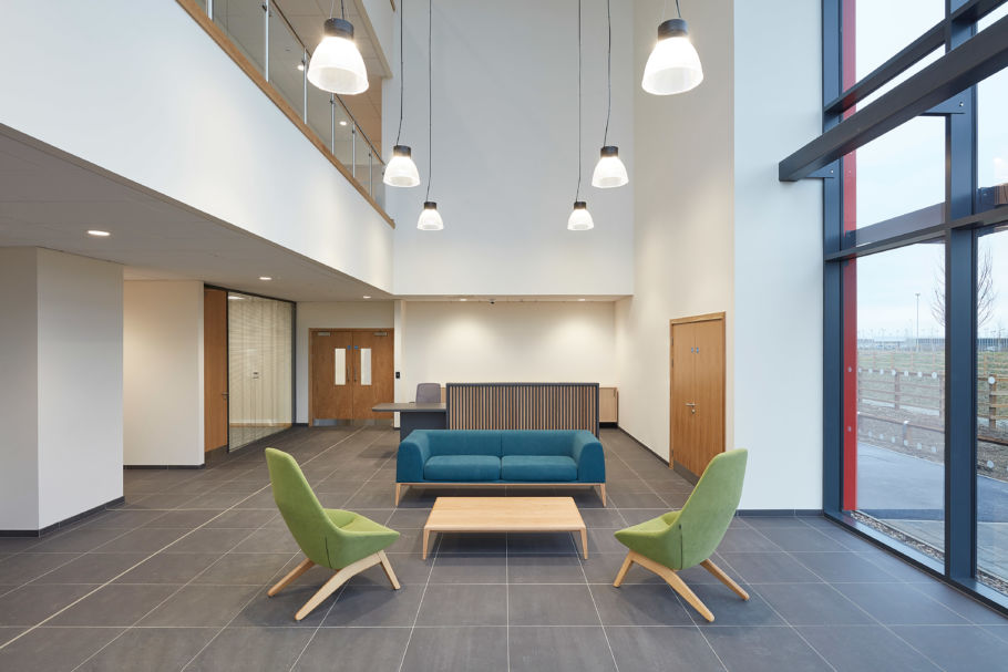 Reception area with two green chairs, one two seater blue sofa with large floor to ceiling windows