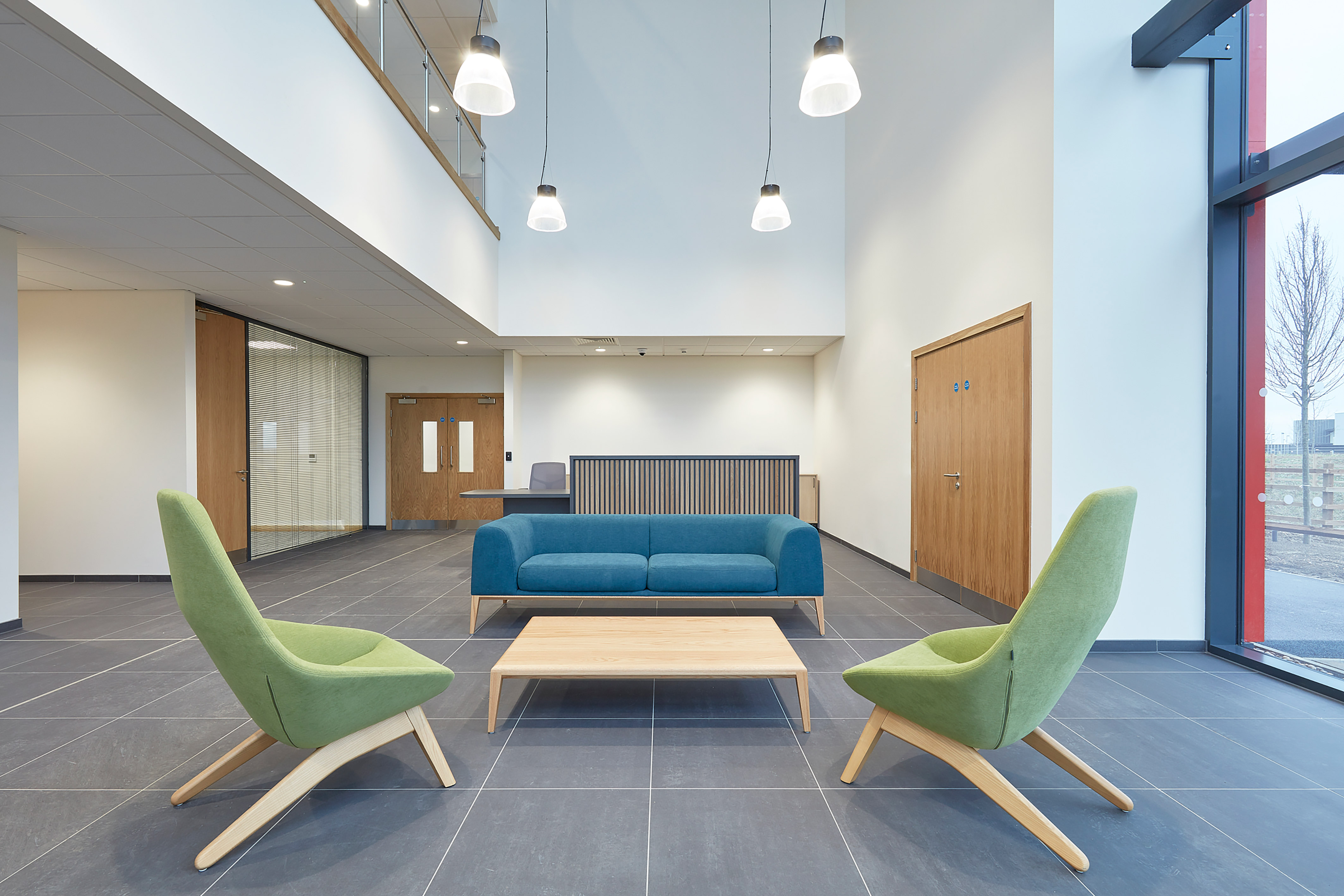 Reception area with two green chairs, one two seater blue sofa with large floor to ceiling windows