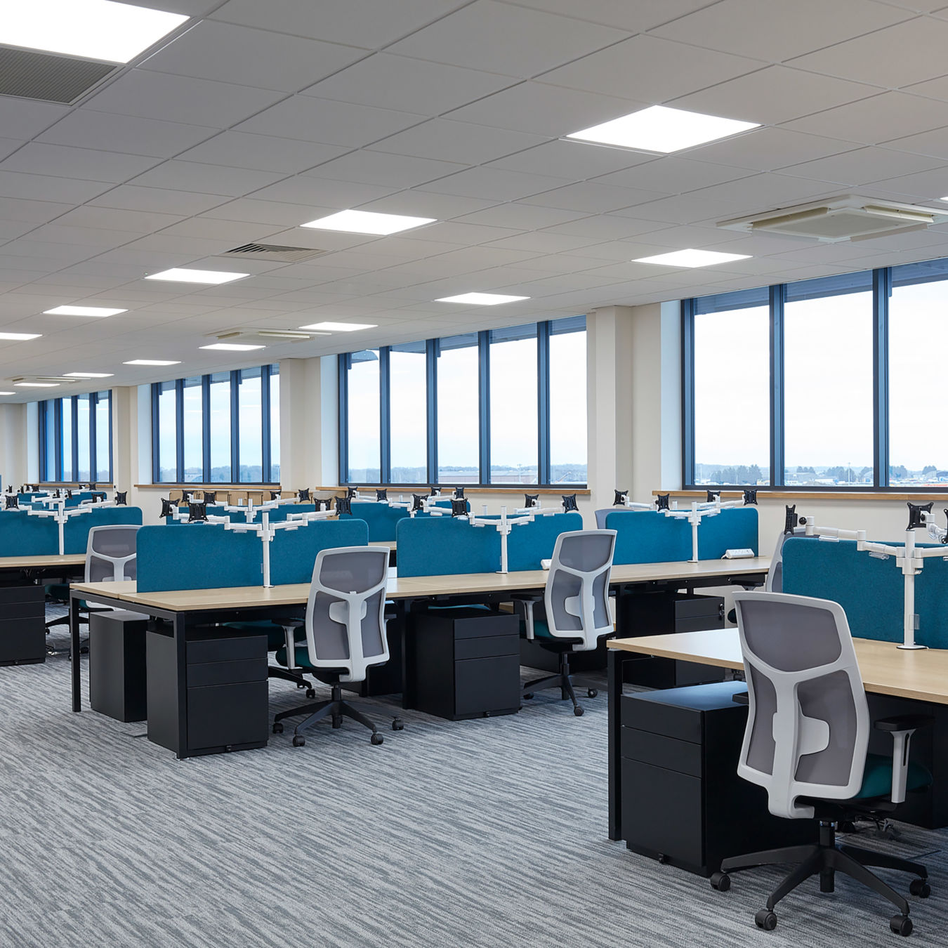 open plan office with multiple desks with blue divider panel a white and blue chair and a filling cabinet under the desk