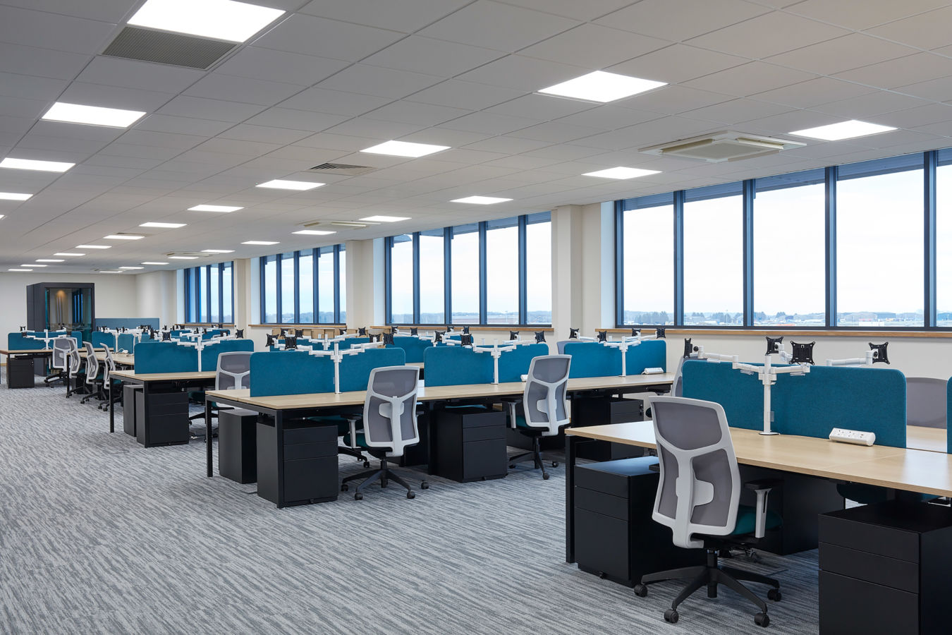 open plan office with multiple desks with blue divider panel a white and blue chair and a filling cabinet under the desk