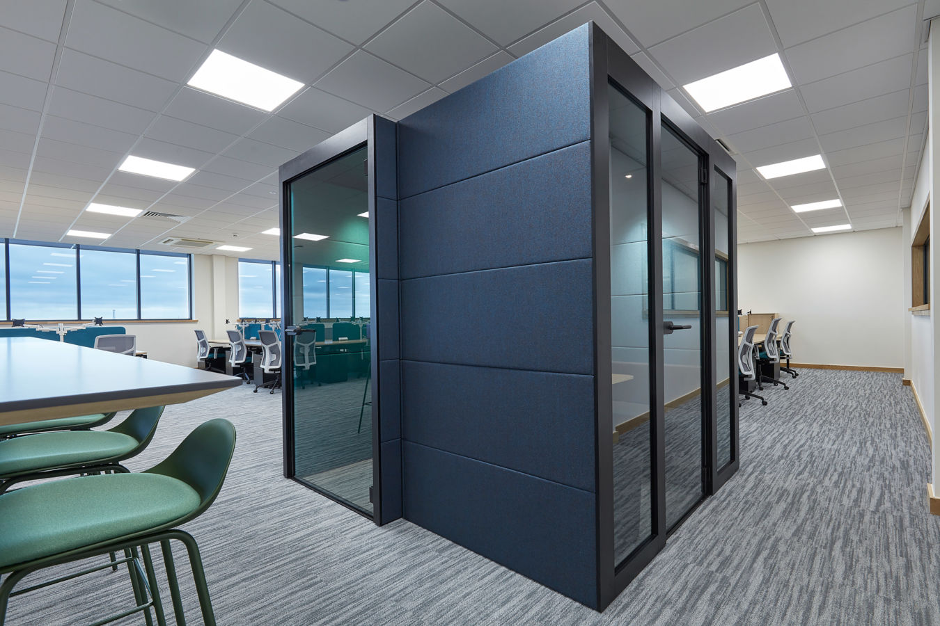 outside of a one person booth, with a wooden panel in the centre, a green stool and dark blue soft walls