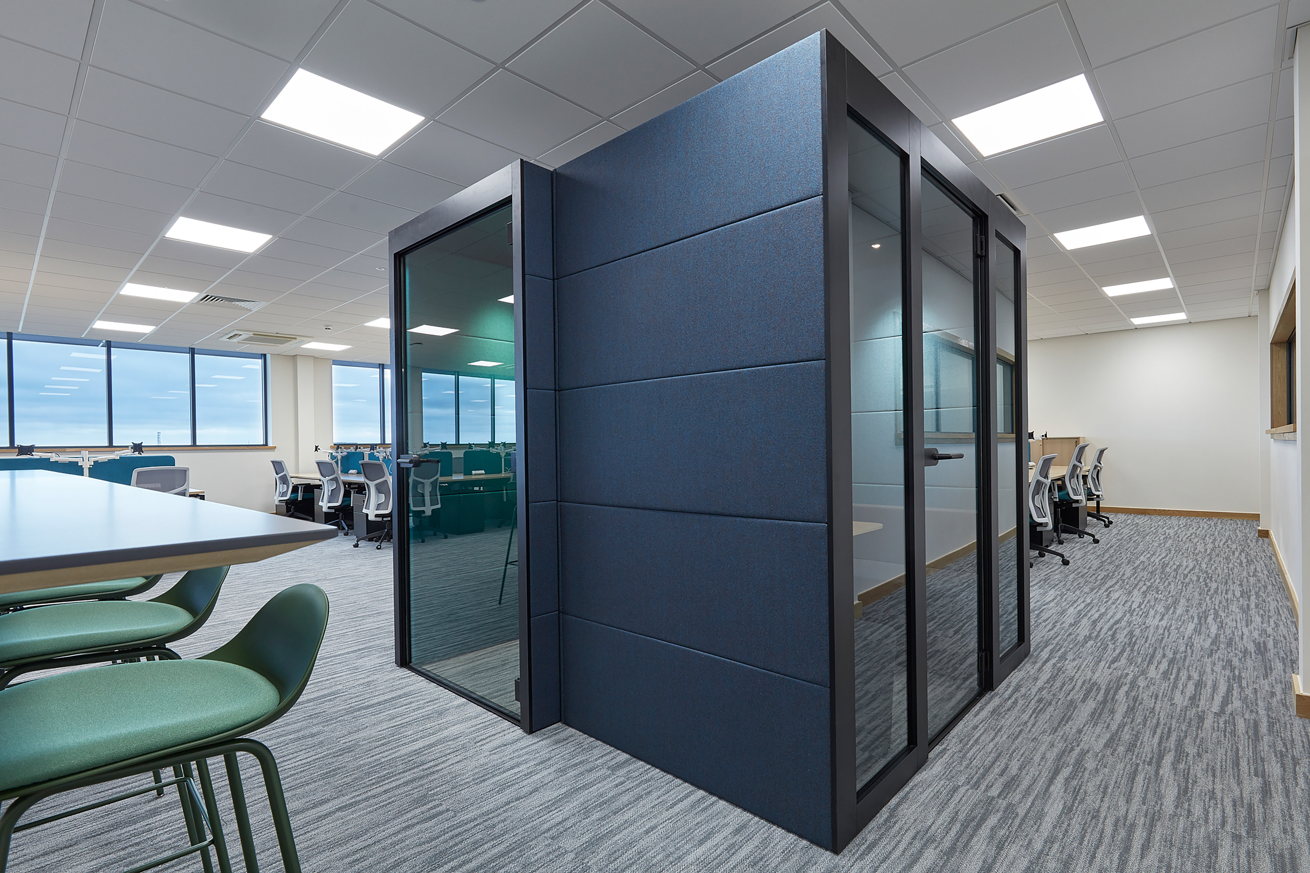 outside of a one person booth, with a wooden panel in the centre, a green stool and dark blue soft walls