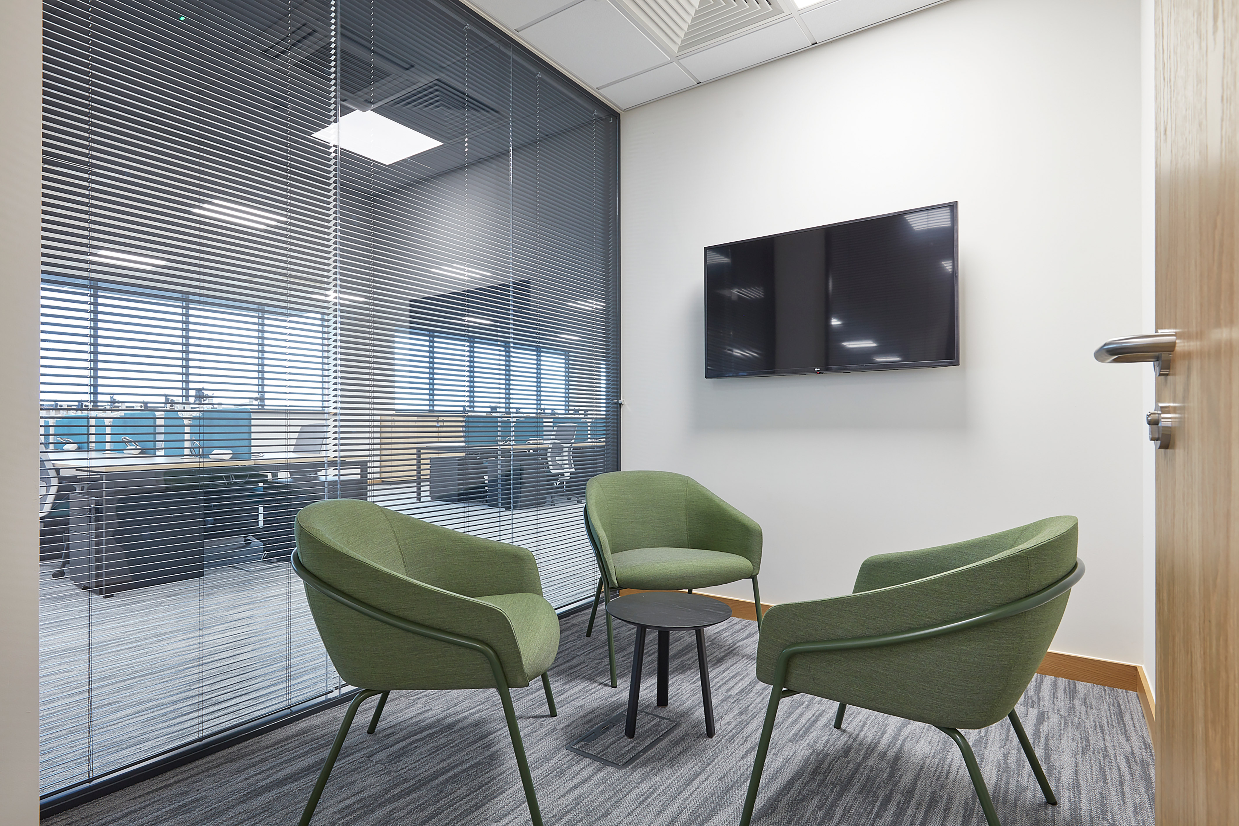 Image of a 3 person collaboration room, with green chairs and a small black table in the centre
