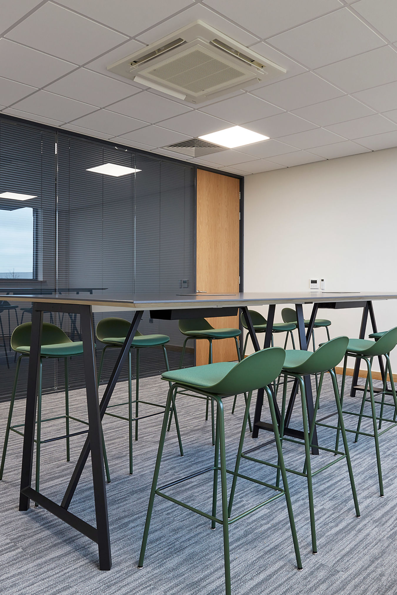 modern conference room with a tall black table and green high stools on a gray carpet. Glass wall, bright lighting, and minimalist design convey a professional tone