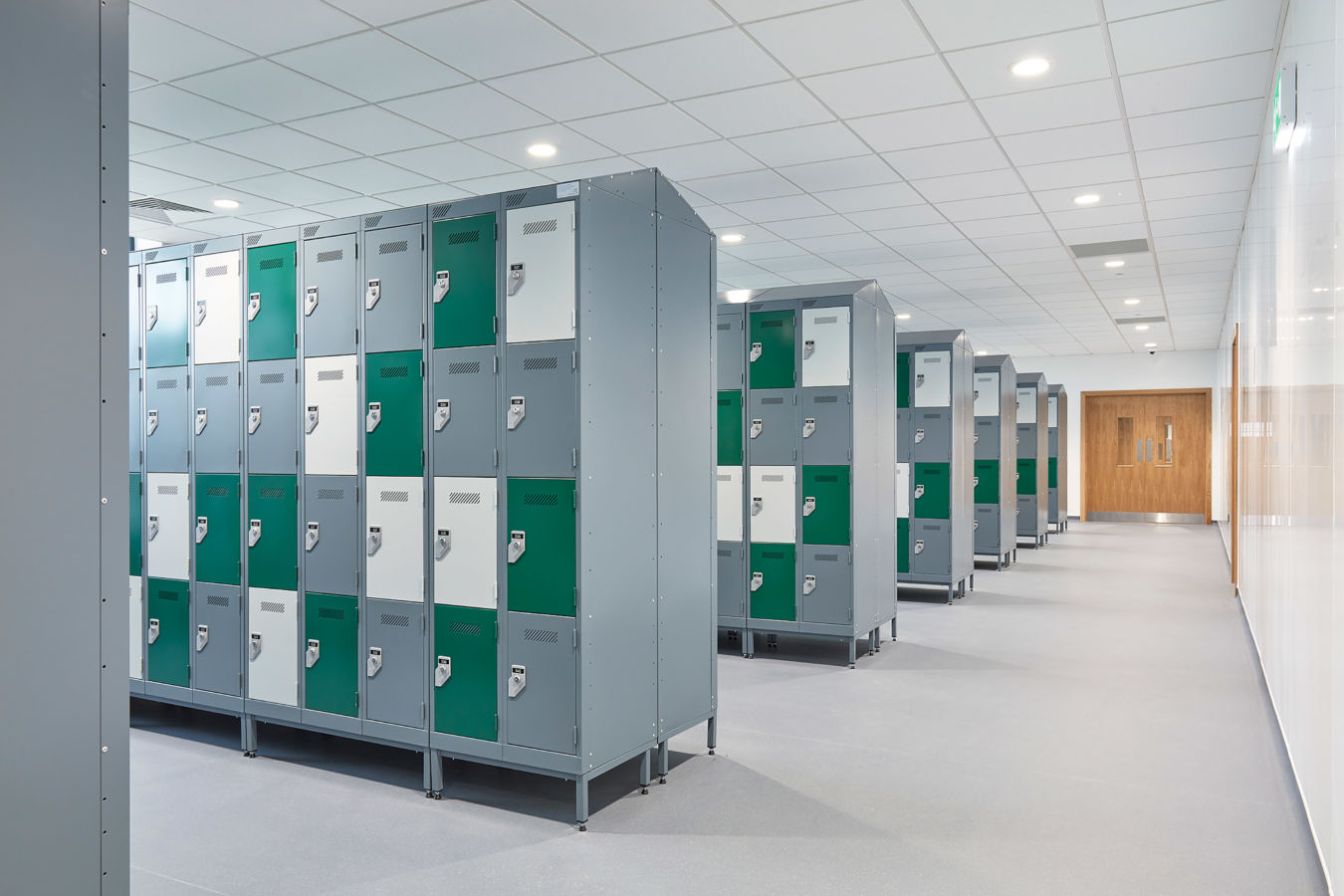 Rows of gray lockers with green and white doors line a bright hallway. The setting is orderly and clean, evoking a sense of modernity and organization.