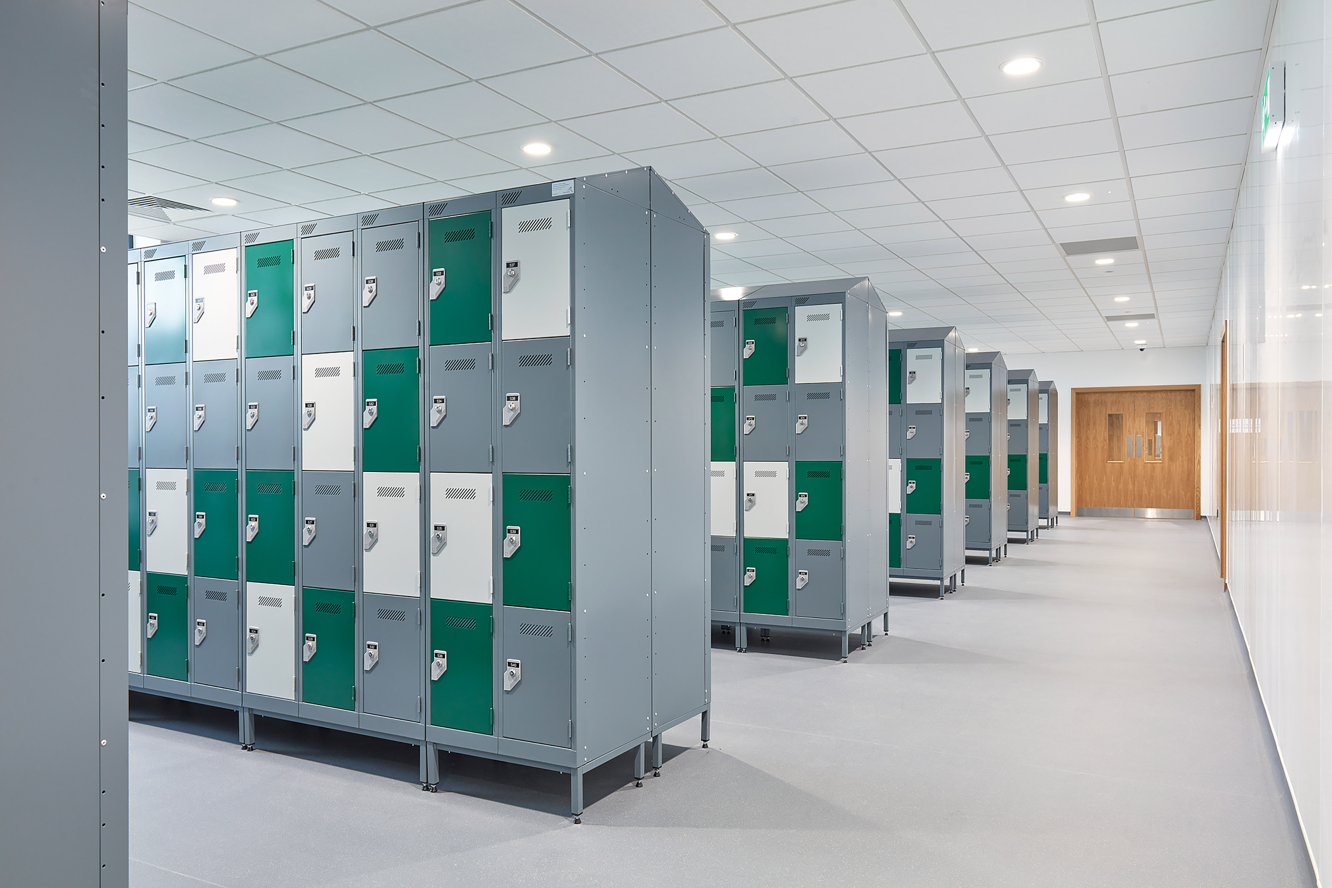 Rows of gray lockers with green and white doors line a bright hallway. The setting is orderly and clean, evoking a sense of modernity and organization.