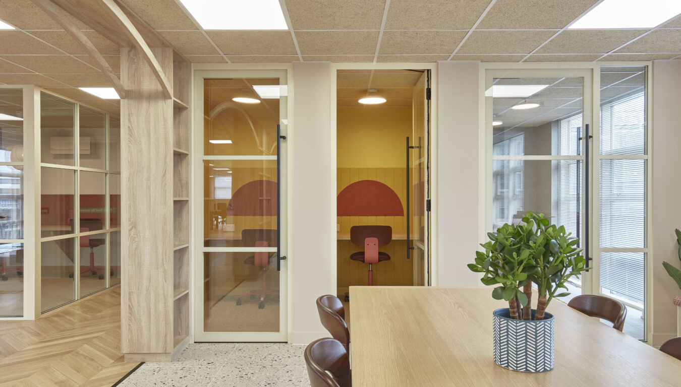 Modern office with glass doors, wooden table, and potted plant. Neutral tones and clean lines create a calm and professional atmosphere.