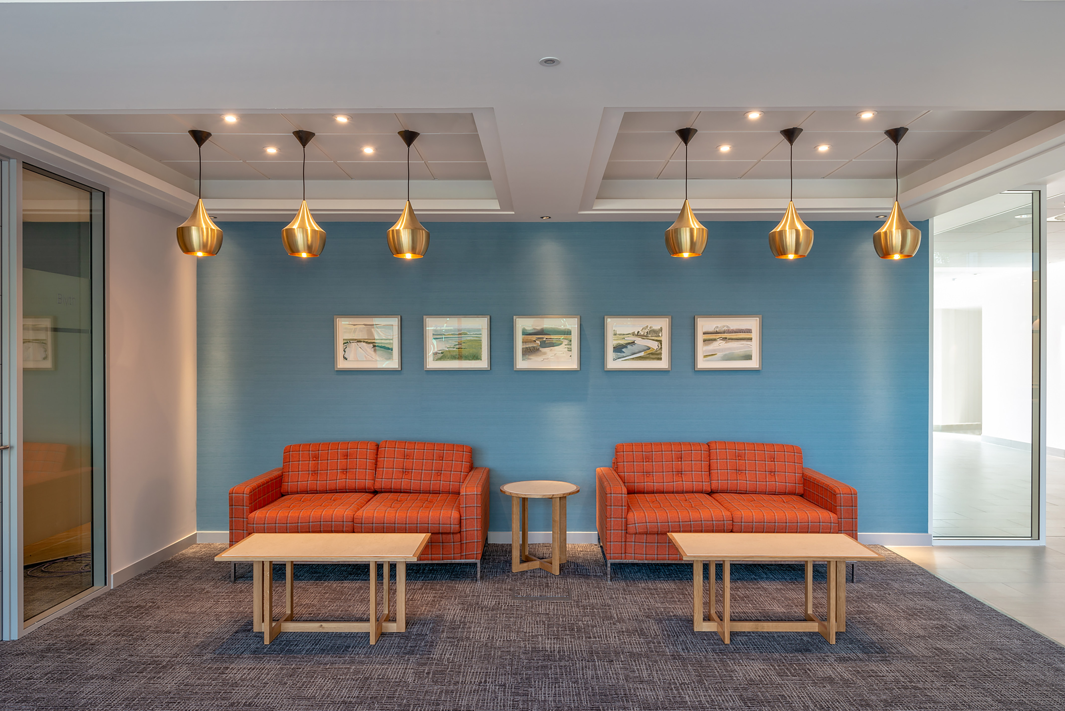 Stylish office lounge with twin orange sofas, pendant lighting, and blue accent wall, part of COEL’s furniture installation for Birketts in Ipswich.
