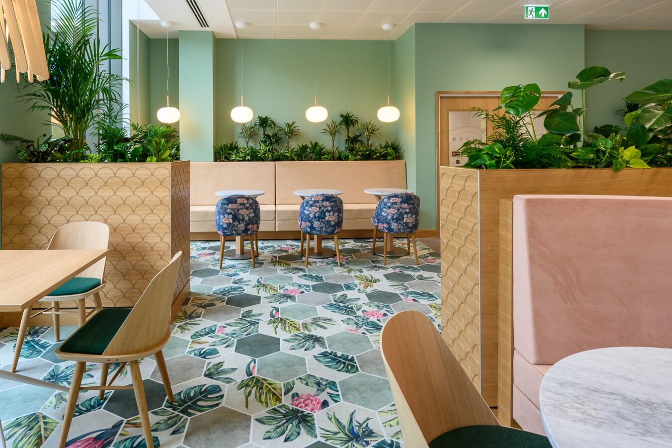 Modern lounge area features beige and teal armchairs around a wooden coffee table with "The Travel Book." Framed artwork decorates the green wall, and a floor lamp provides warm lighting.