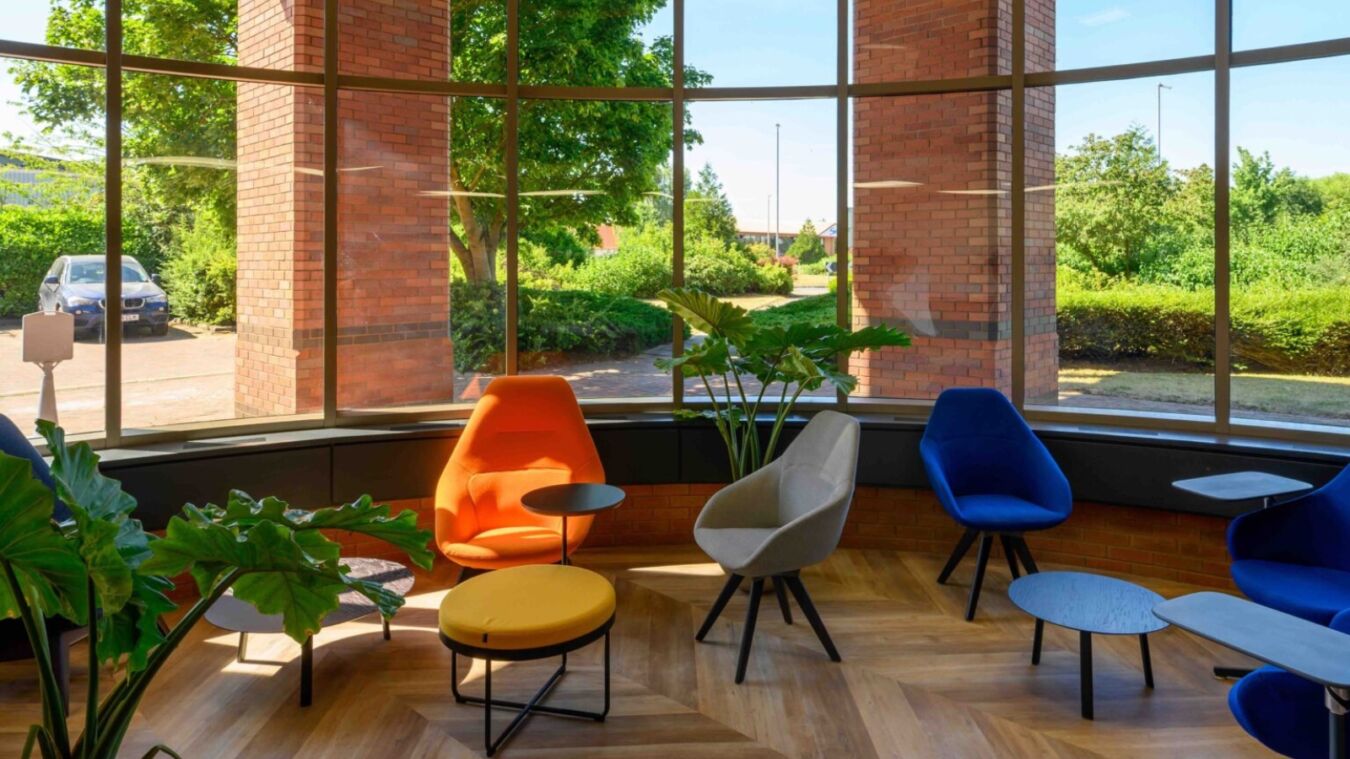 Colourful lounge area with modern chairs and tables, large windows, indoor plants, and a view of a green outdoor space